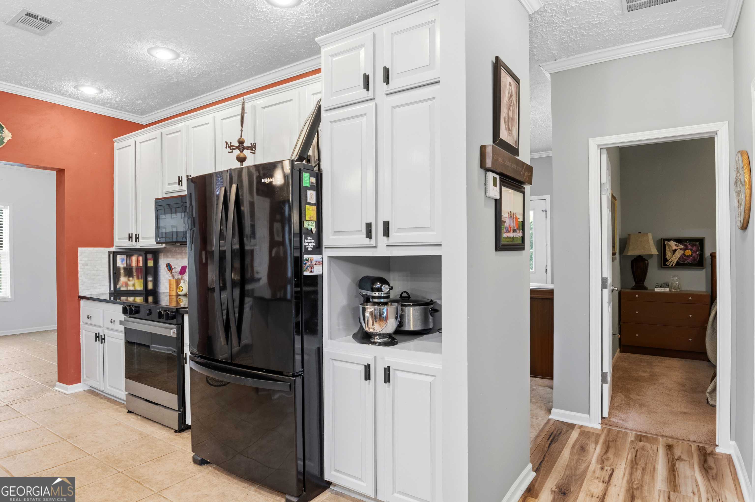 Kitchen with white cabinets, black appliances, and a countertop mixer beside an adjoining hallway.