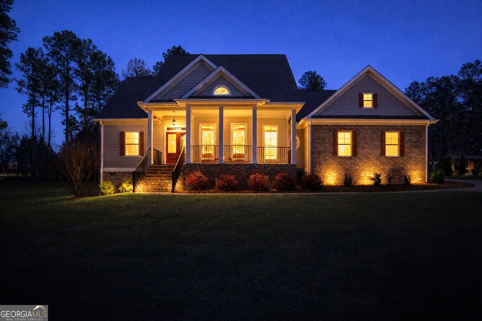 Gabled home at night with a columned porch, brick facade, and warmly lit windows.