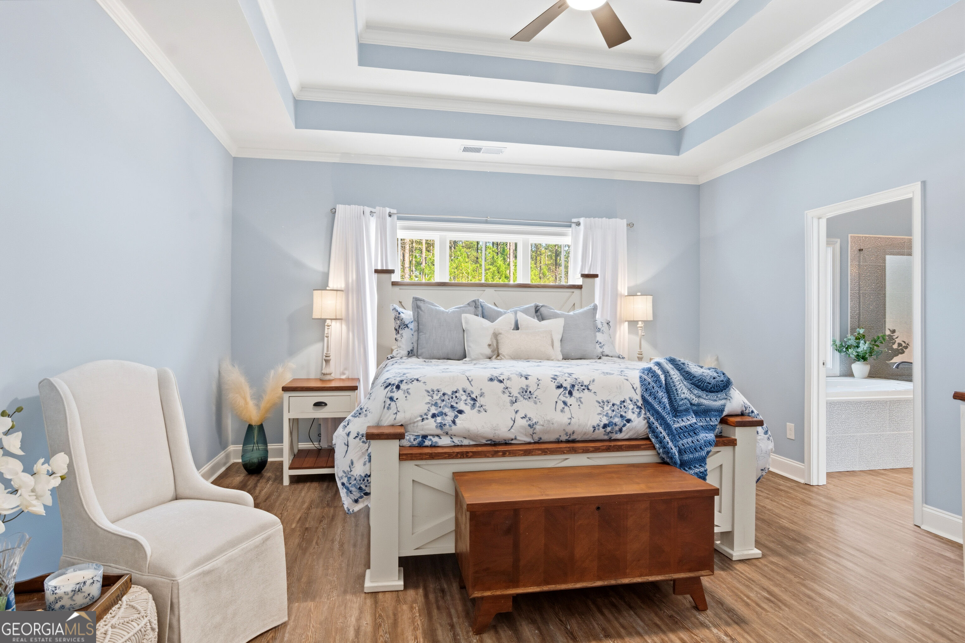 Bedroom with blue floral bedding, a tray ceiling, and an adjoining bathroom visible through the doorway.