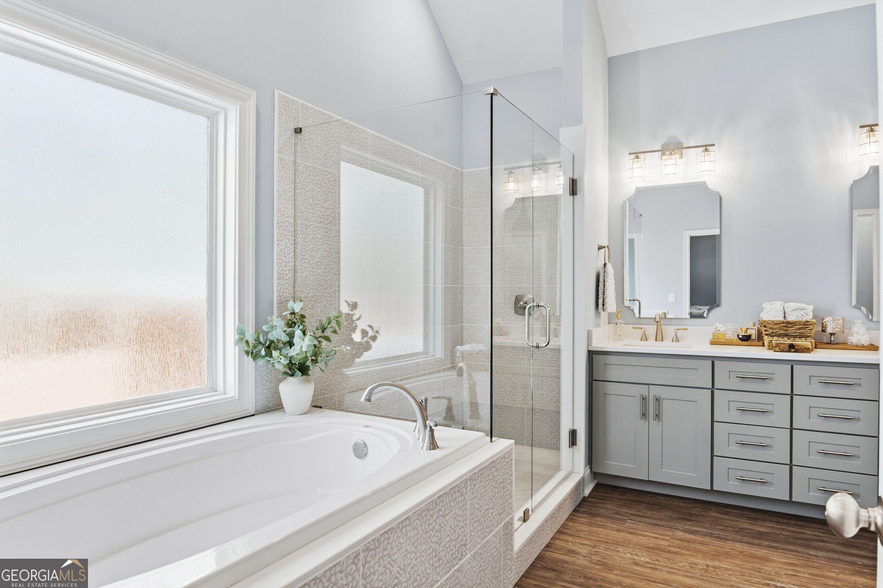 Bathroom with a built-in soaking tub, glass shower, patterned tile, and gray double vanity.