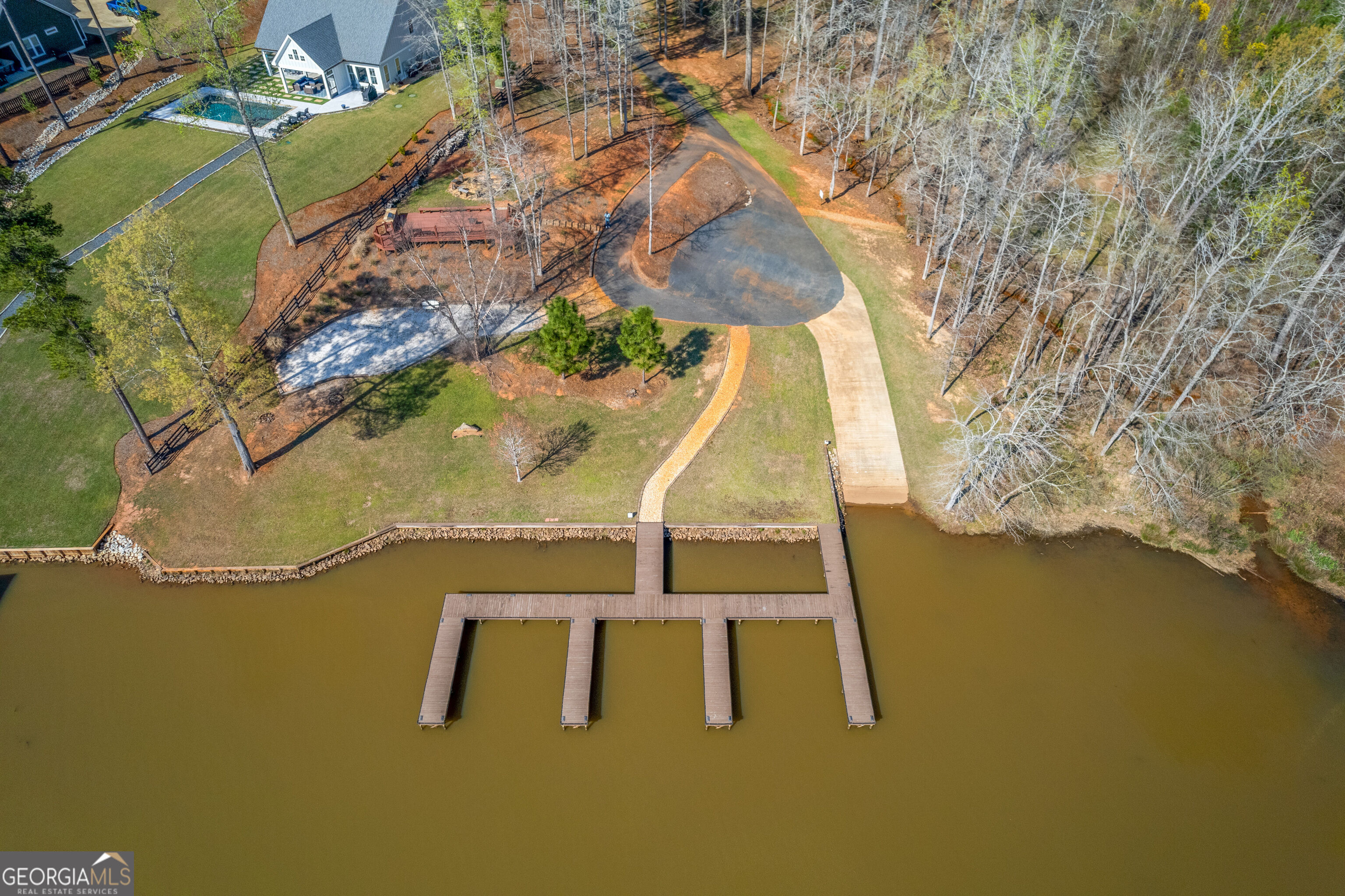 Aerial view of a lakefront property with a multi-slip dock, curving driveway, and landscaped lawn.