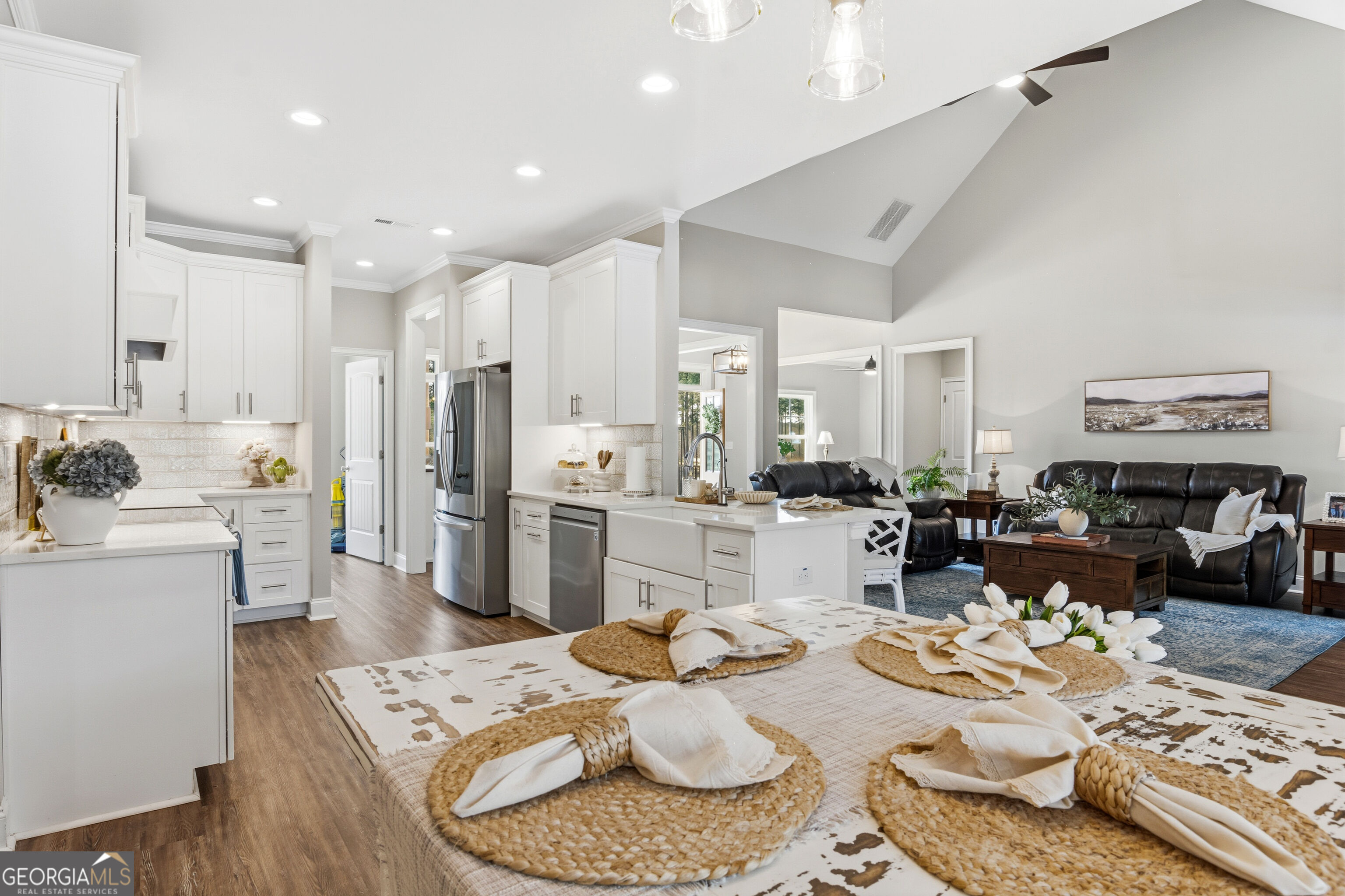 Open-plan kitchen and living room with a large white island, vaulted ceiling, and black leather sofas.