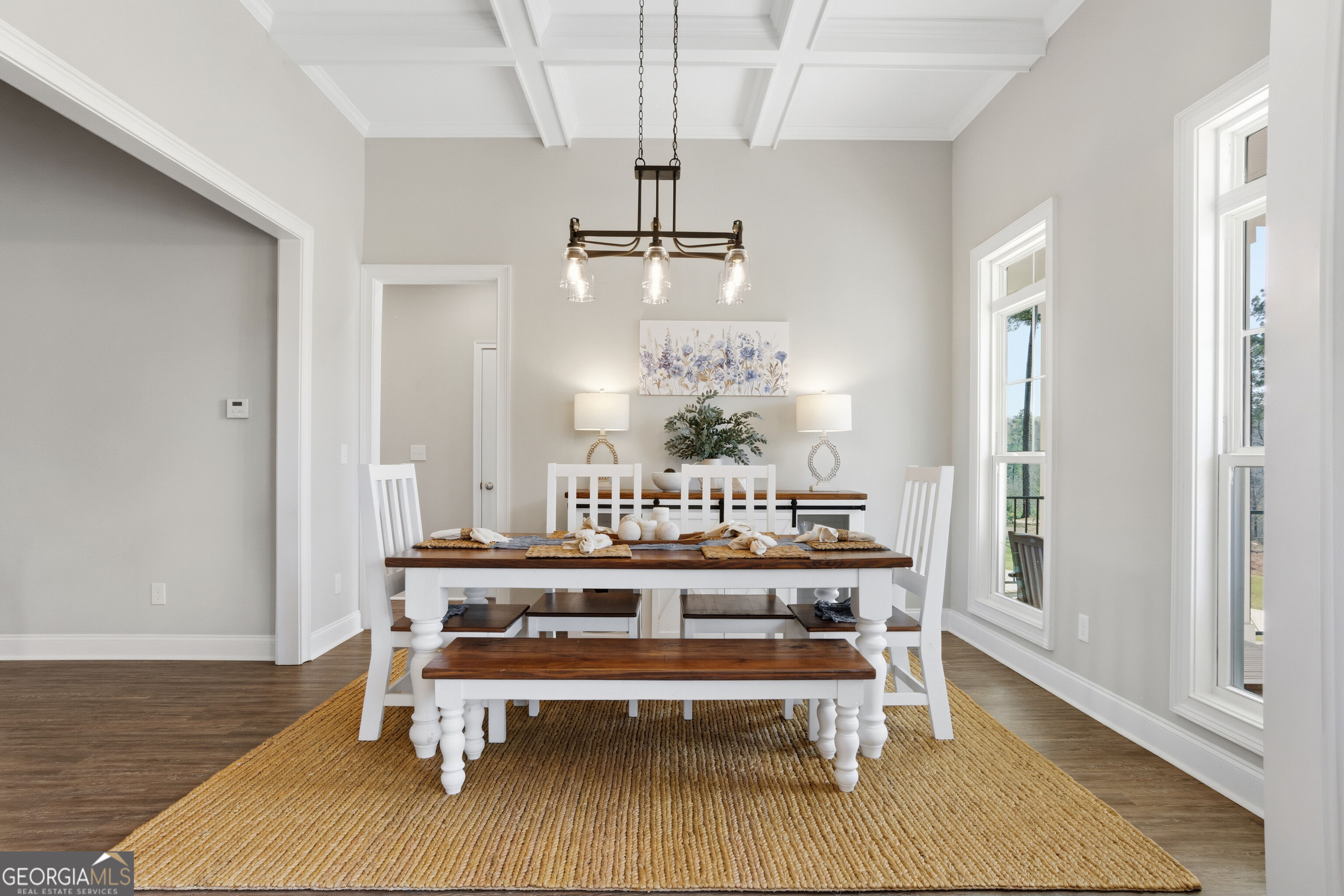 Staged dining room with a white table, wood benches, woven rug, and tall windows.
