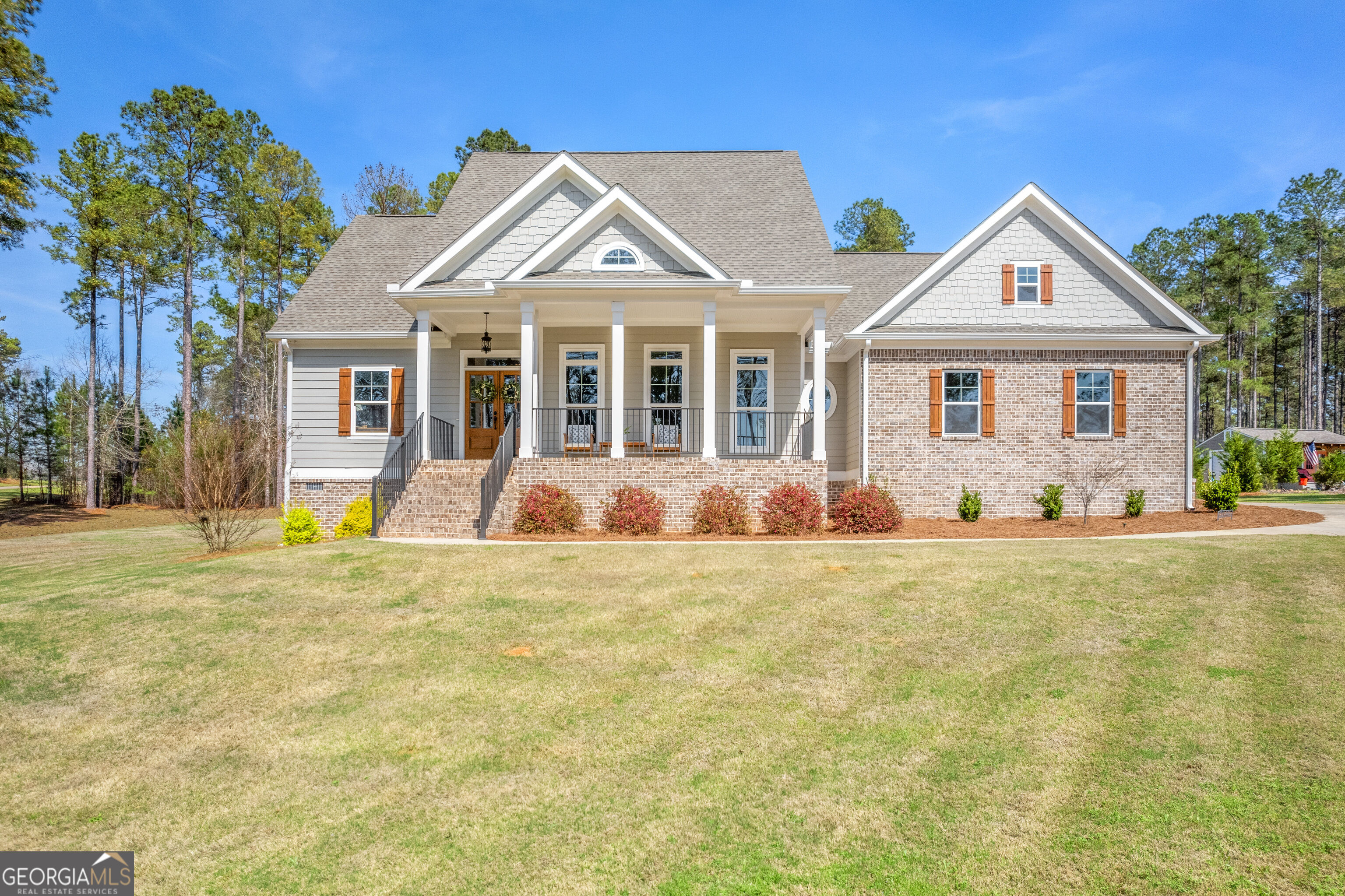 Gray-and-brick home with a covered front porch, brick steps, and a broad lawn.