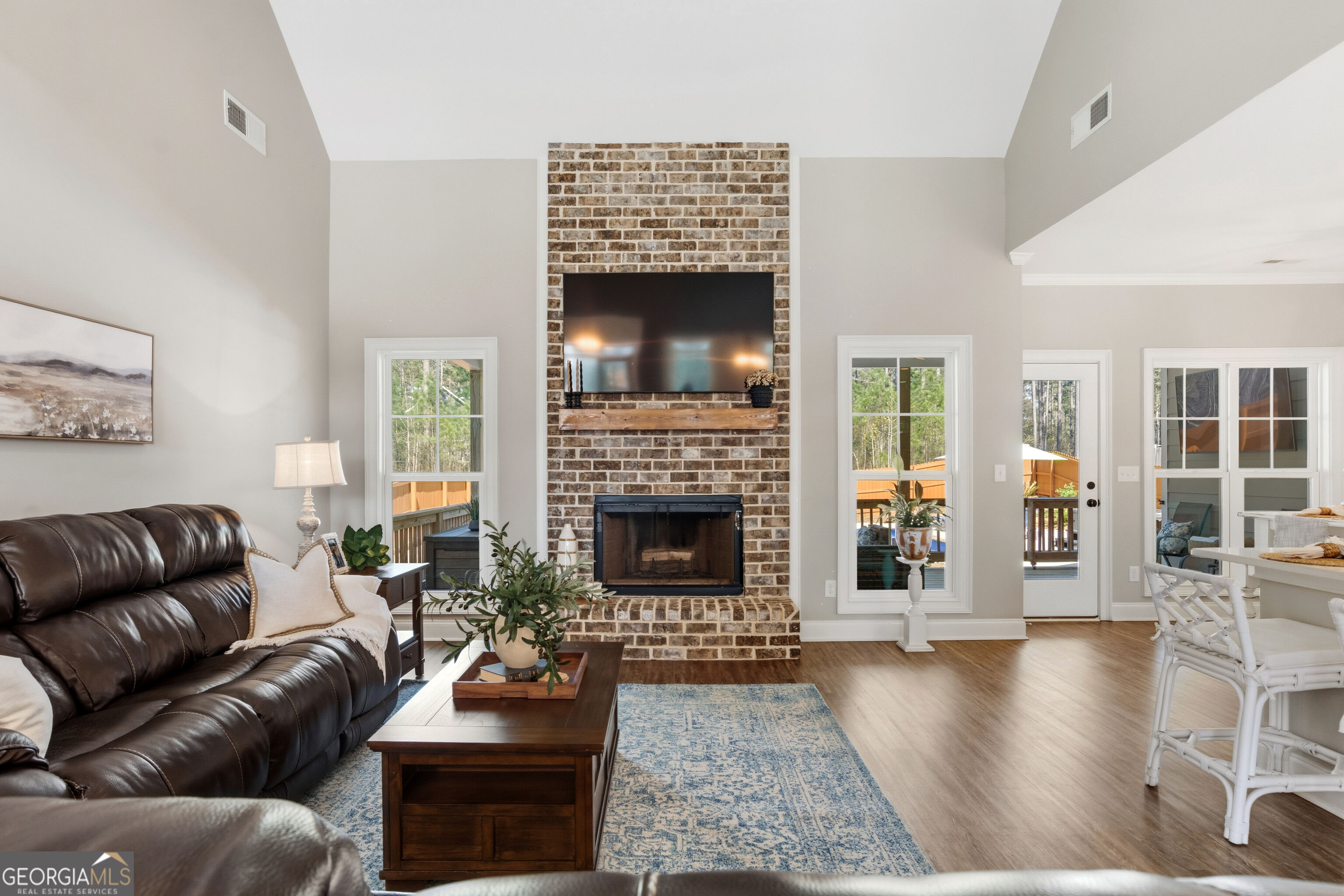 Living room with a tall brick fireplace, mounted television, leather sofa, and blue patterned rug.