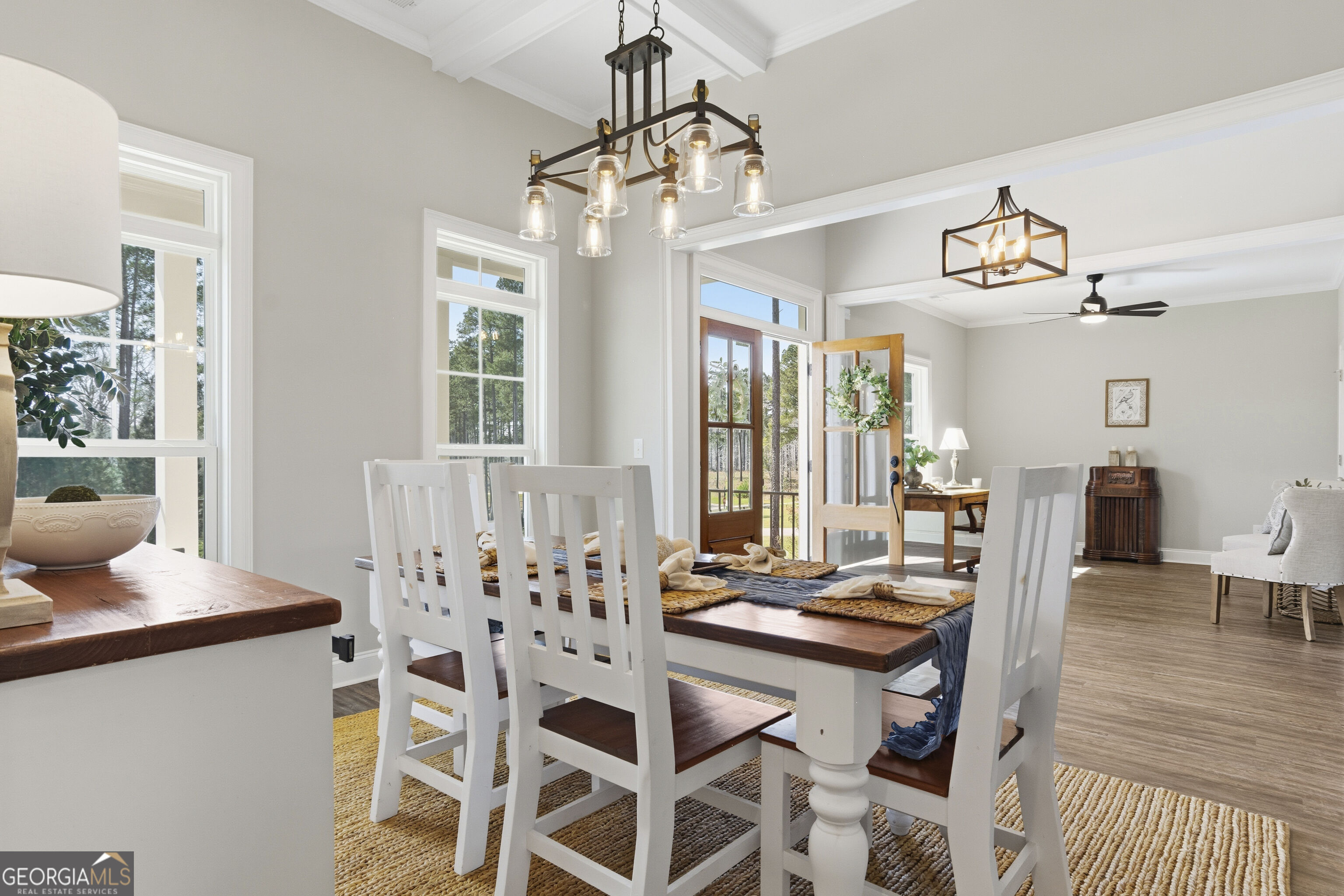 Dining room with a dark wood table, white chairs, large windows, and glass-paneled doors.