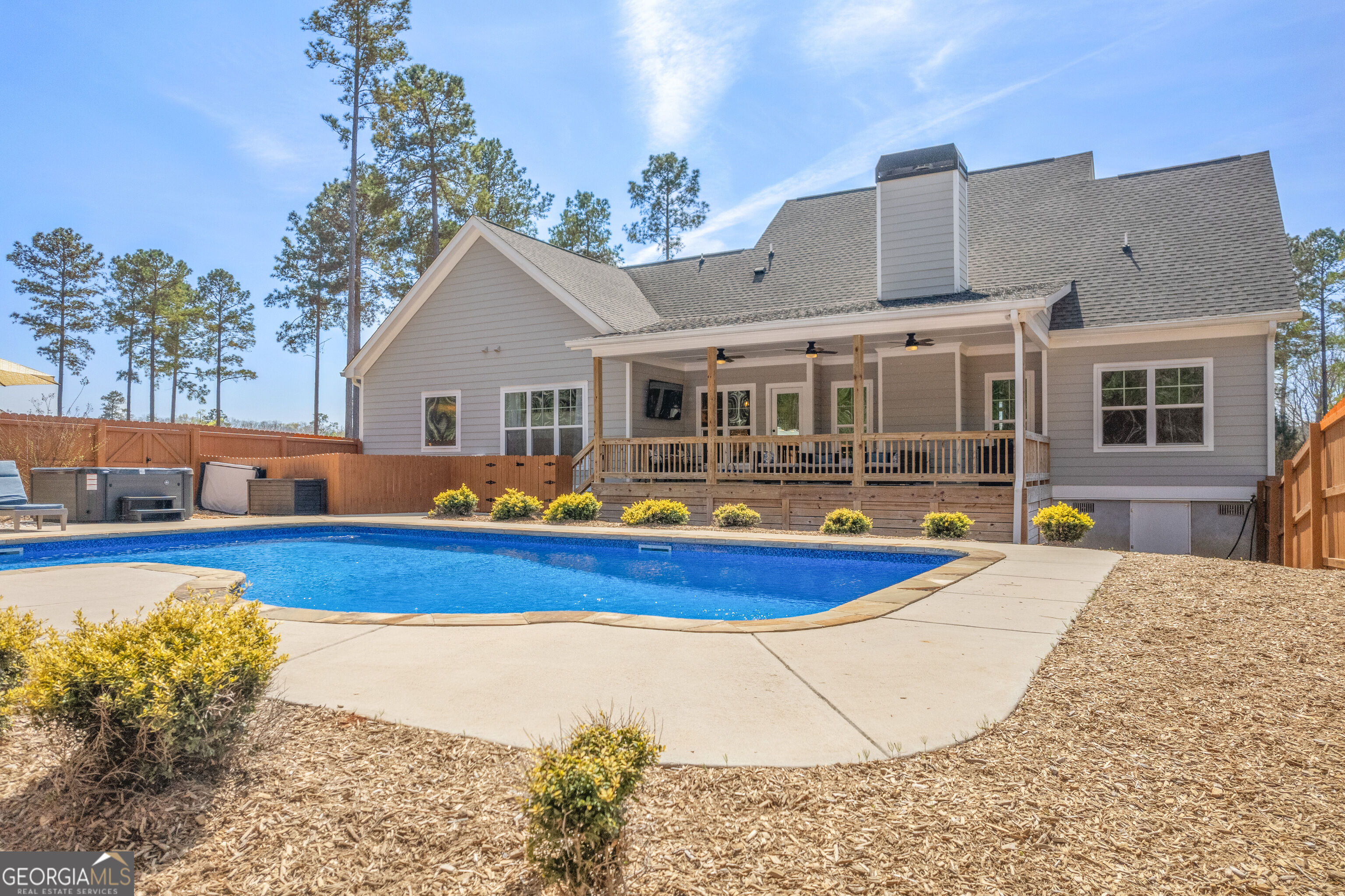 Home’s covered rear deck overlooks a blue in-ground pool in a fenced backyard.