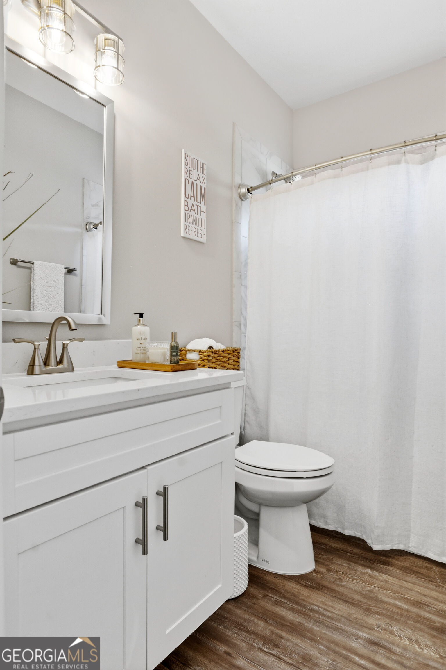Bathroom with a white vanity, chrome fixtures, shower curtain, and warm wood-look flooring.
