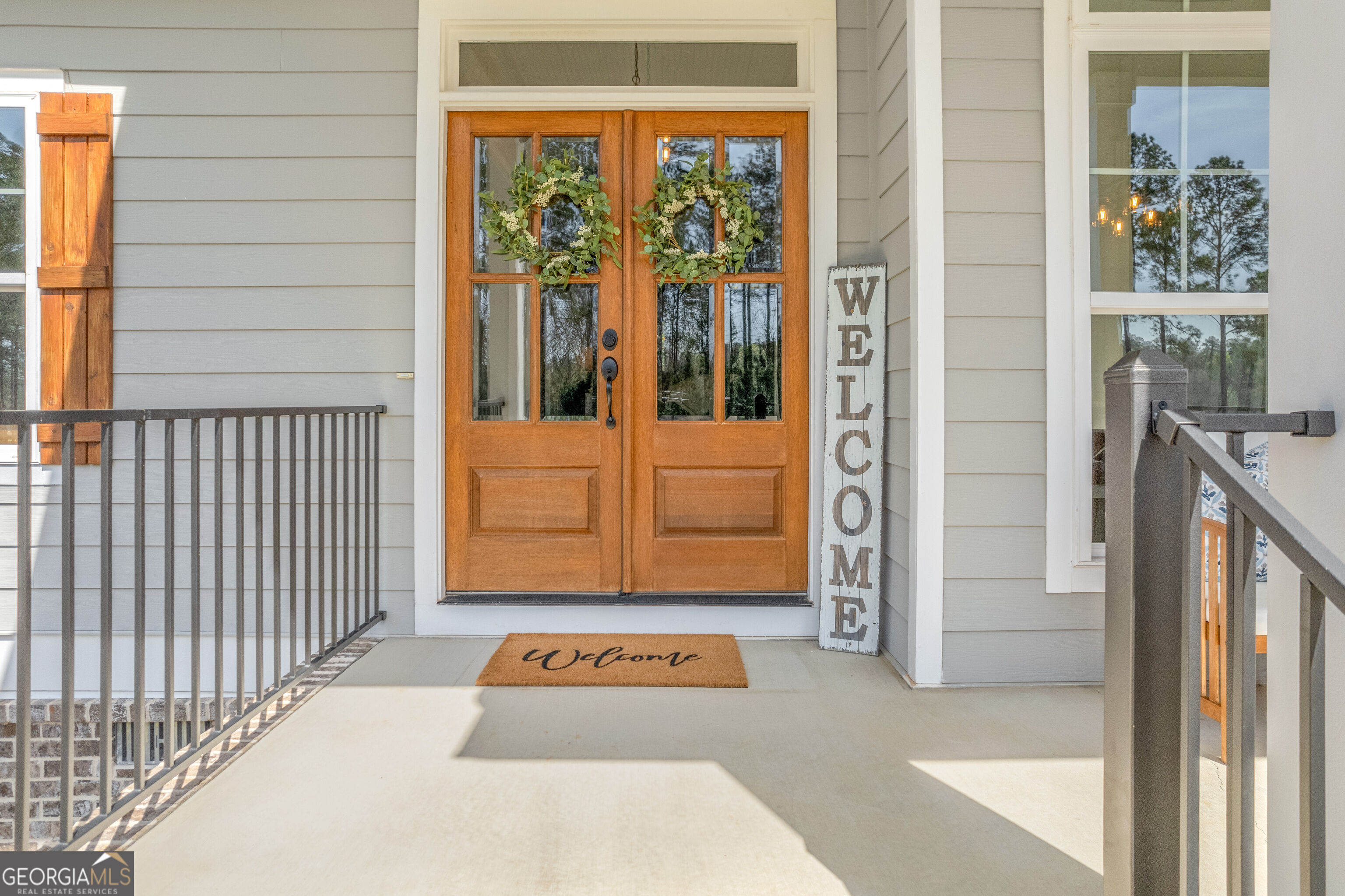 Covered porch entrance with wood double doors, matching wreaths, and welcome signs.