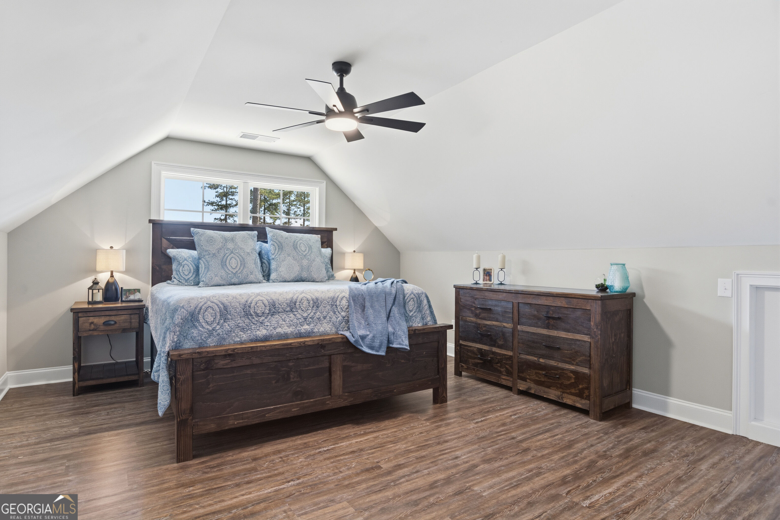 Attic bedroom with a dark wood bed, blue patterned bedding, matching dresser, and sloped ceiling.