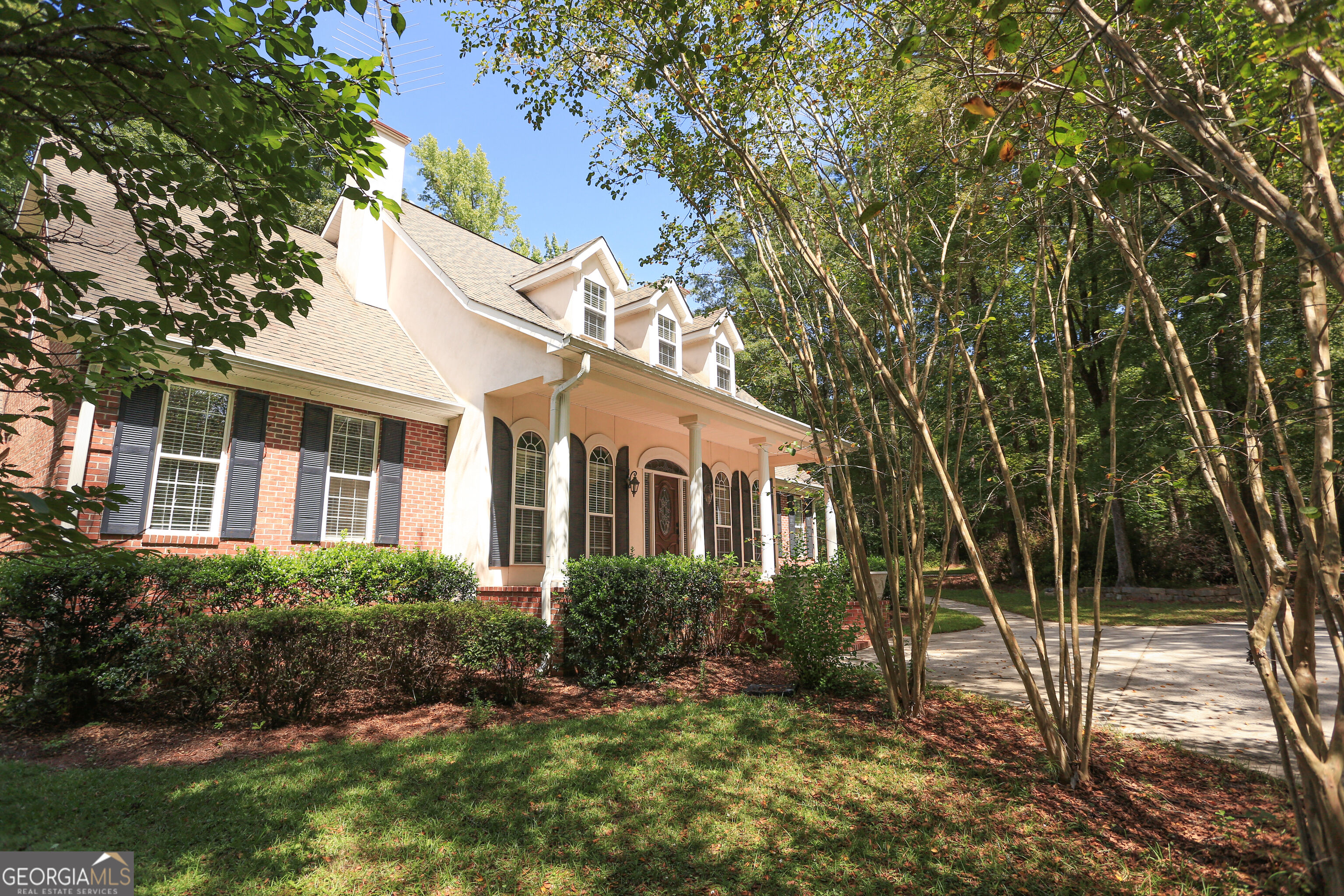 Two-story brick and stucco home with a columned porch, dormer windows, and a tree-lined driveway.