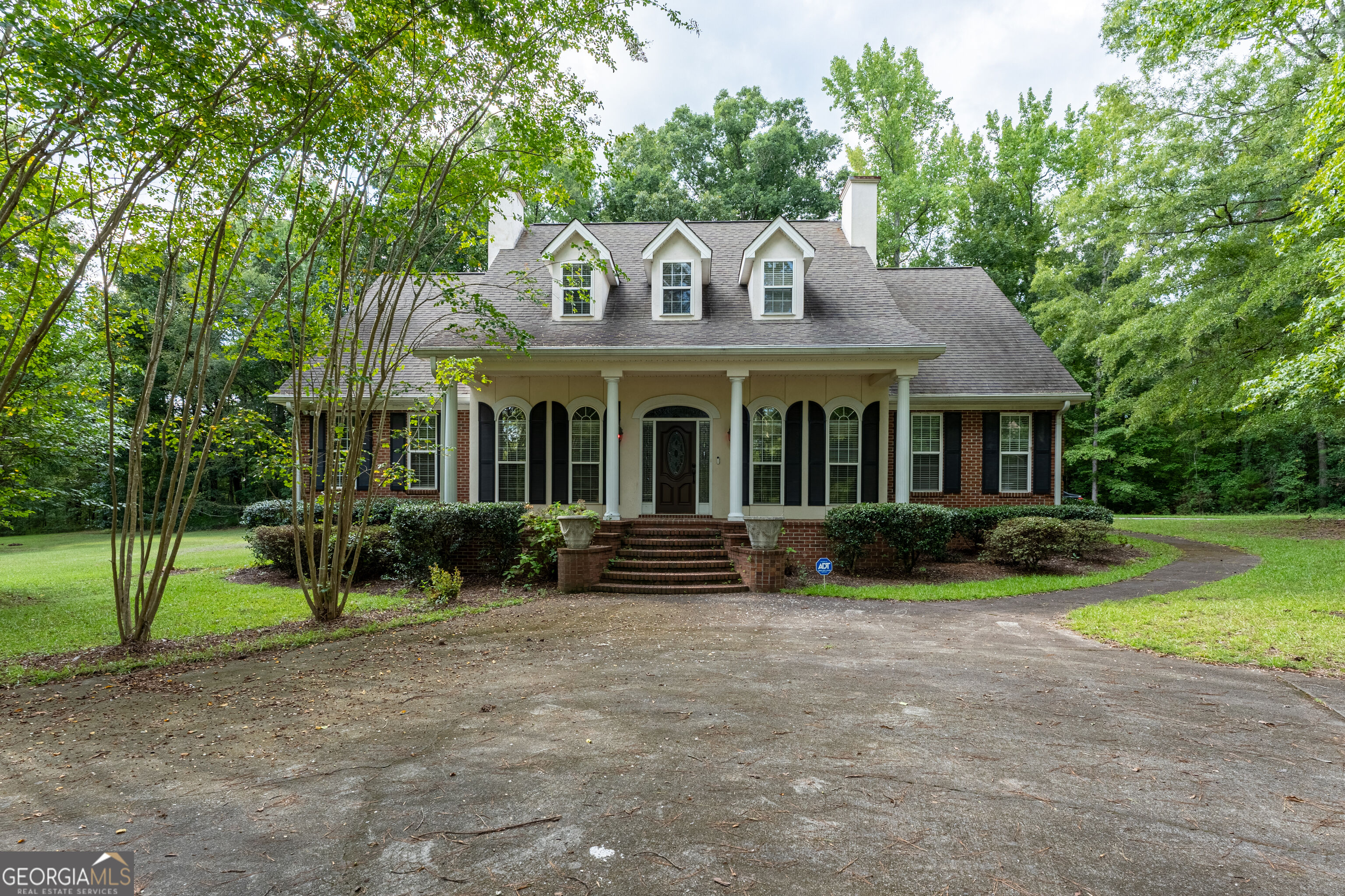 Home with three roof dormers, a columned front porch, brick accents, and a curved driveway.