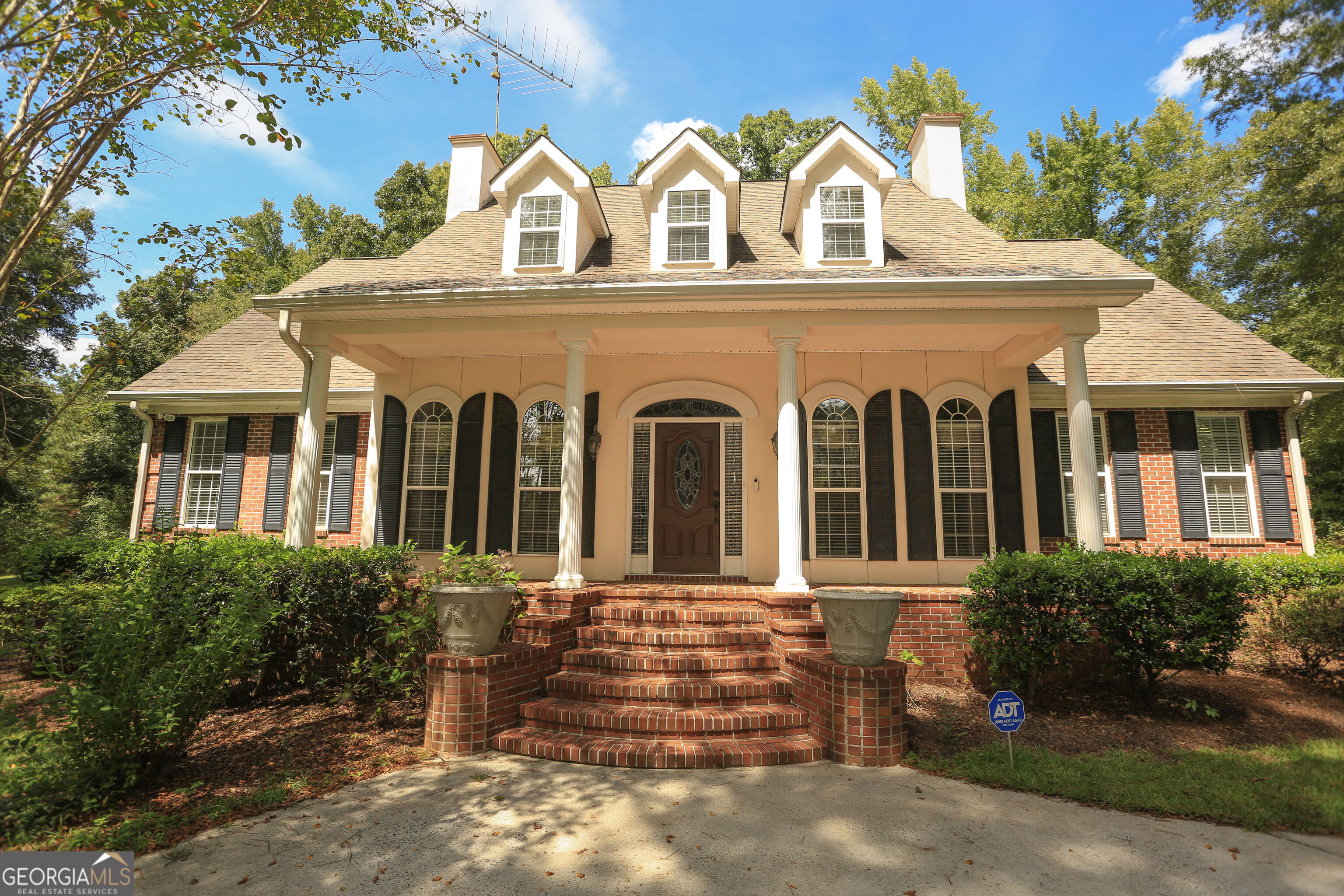 Brick house with a columned porch, three dormers, and curved brick steps.