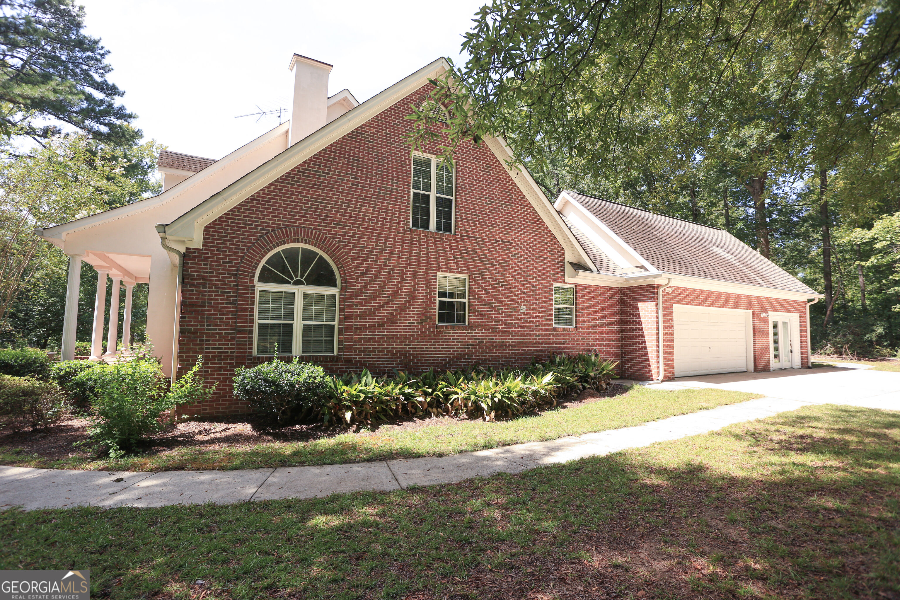 Red brick house with an arched window, covered porch, attached garage, and mature trees.