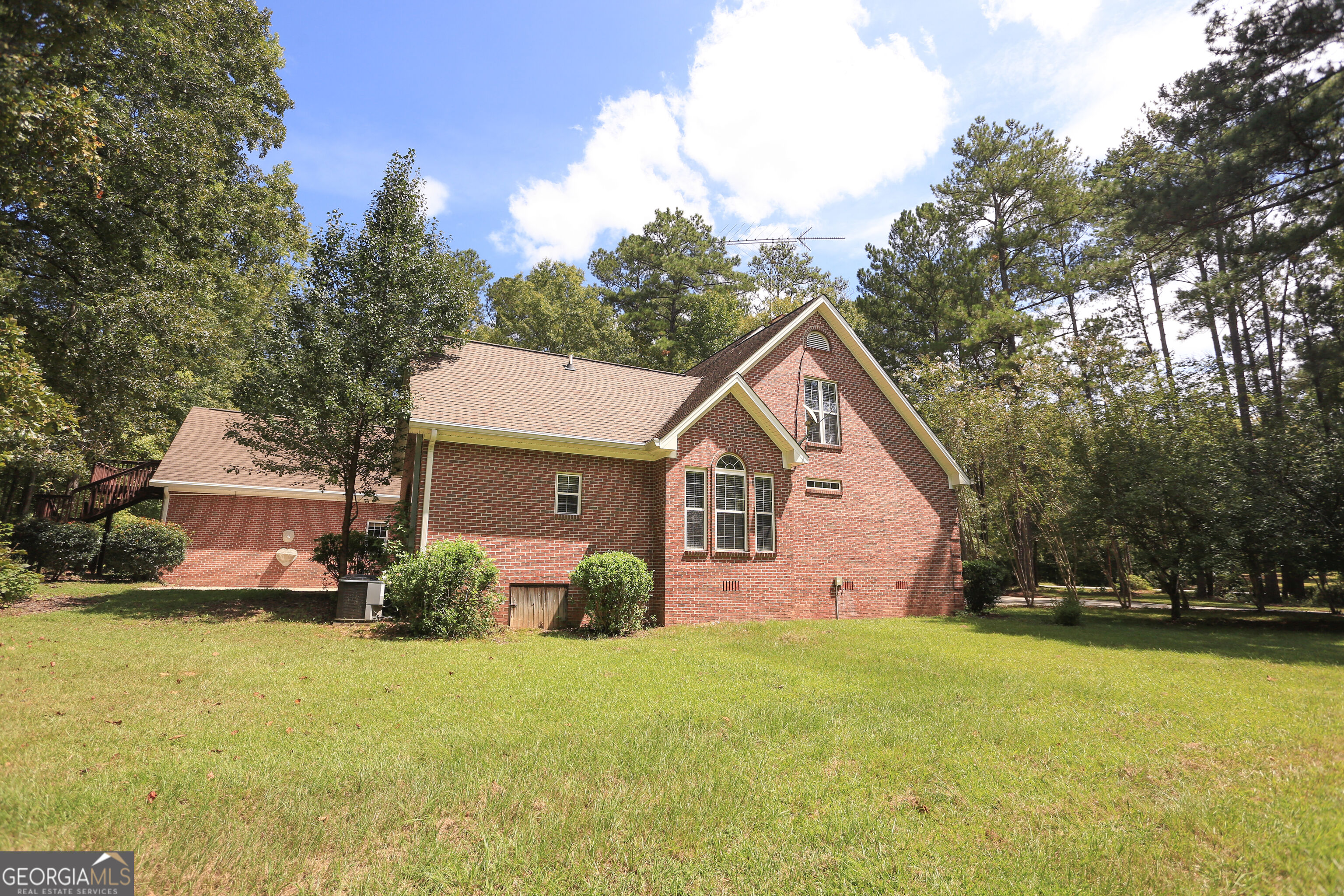 Red brick house with a tall gable, elevated deck, and wooded lawn.