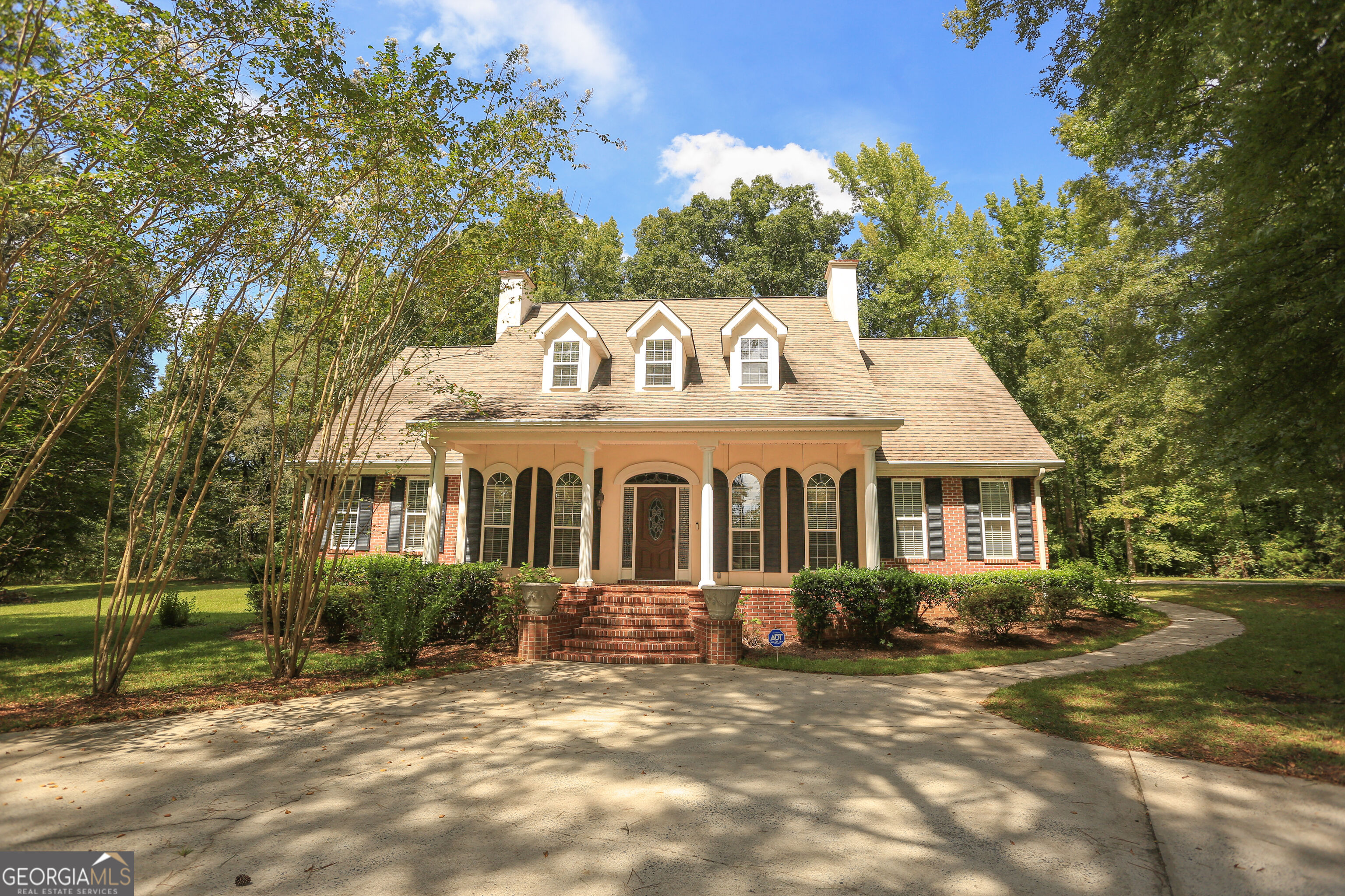 Brick-and-cream house with three front dormers, a columned porch, and a curved driveway.