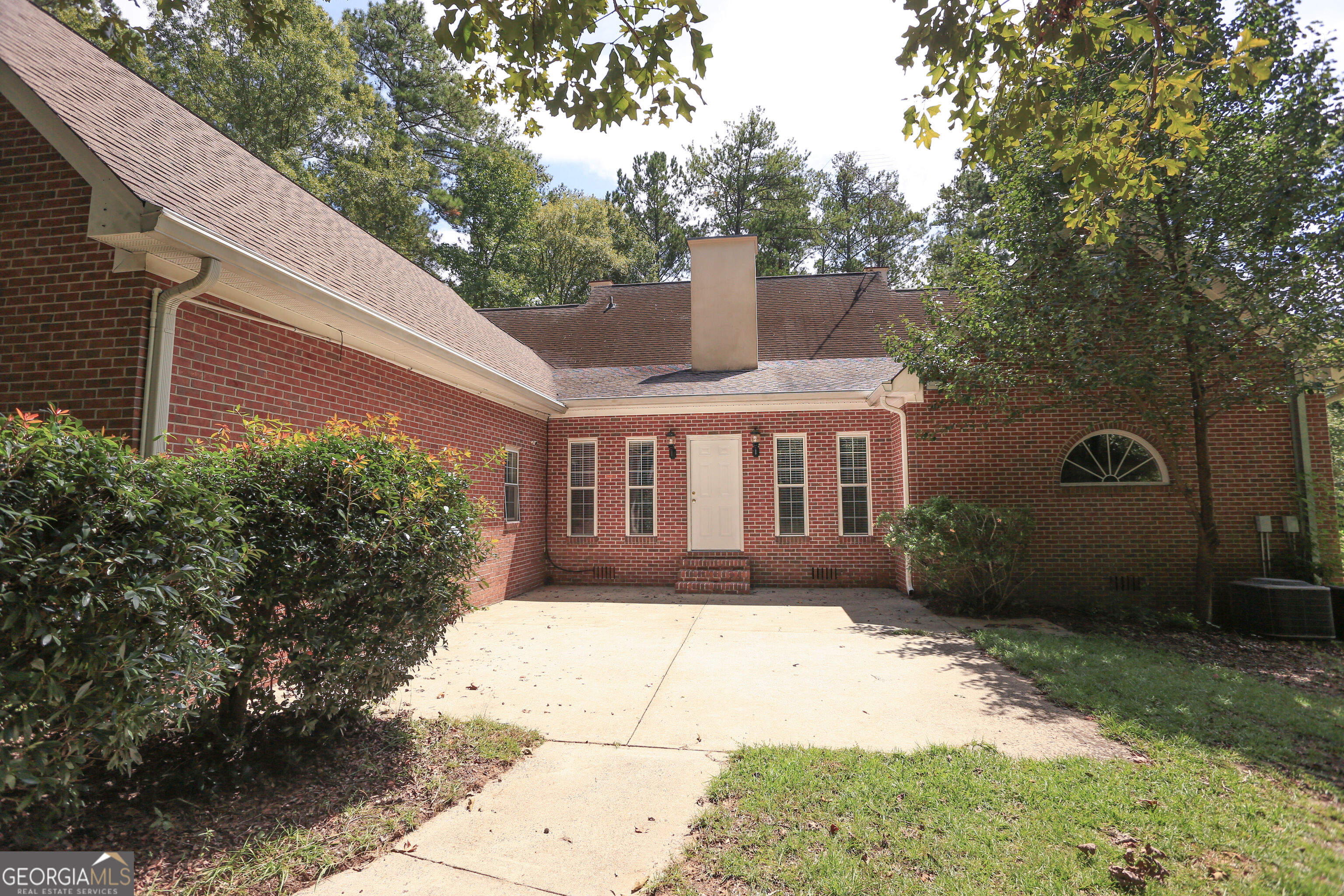 Red-brick home’s rear patio with a white door, tall windows, and mature landscaping.