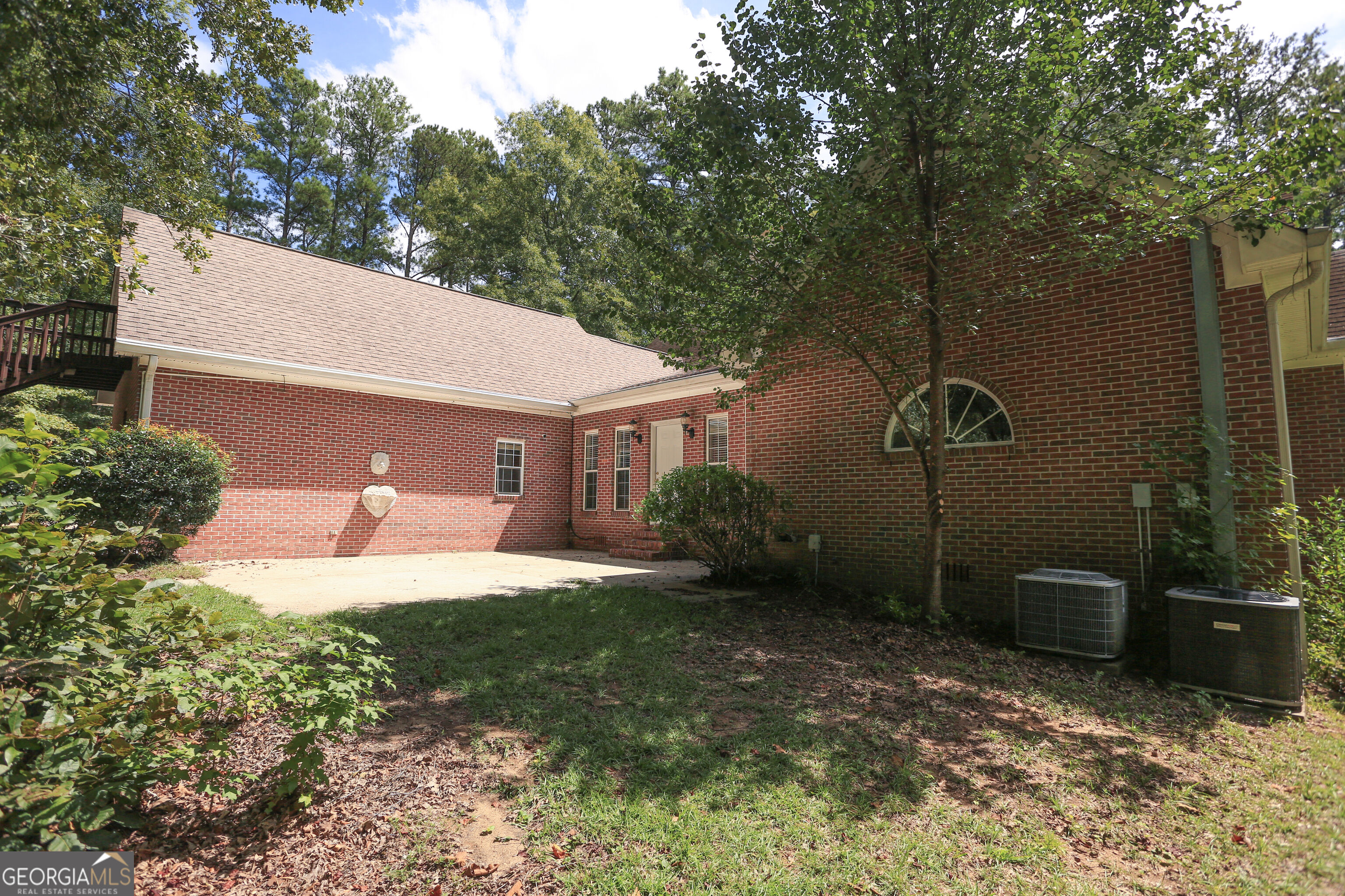 Red brick home’s shaded rear patio beneath mature trees, with two outdoor air-conditioning units.