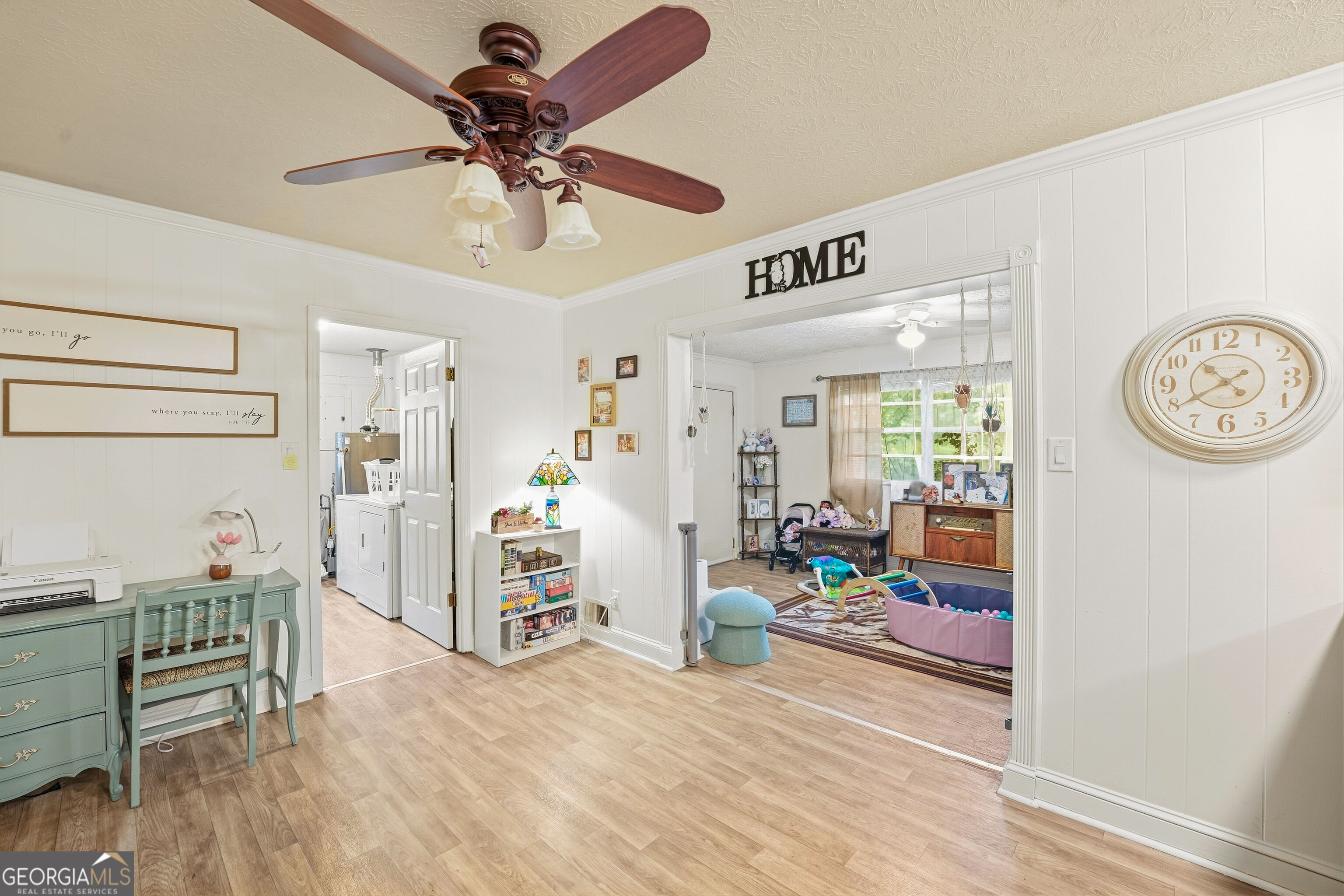 Furnished interior with a mint-green desk and a children’s play area through a wide doorway.