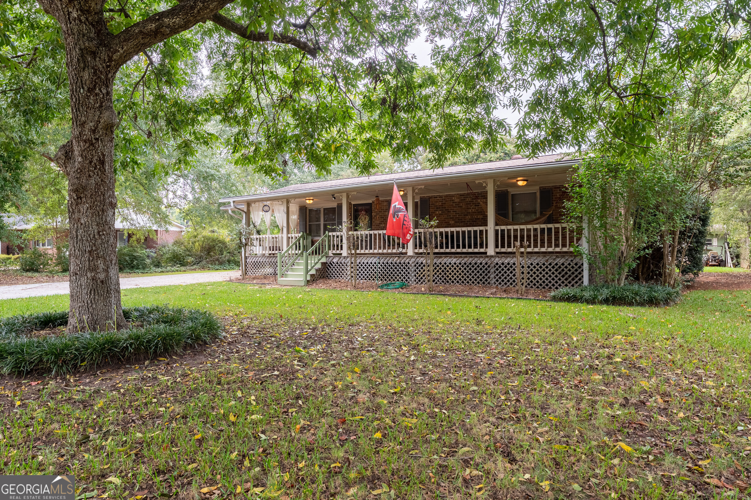 Brick home with a long covered porch and green steps beneath a large shade tree.