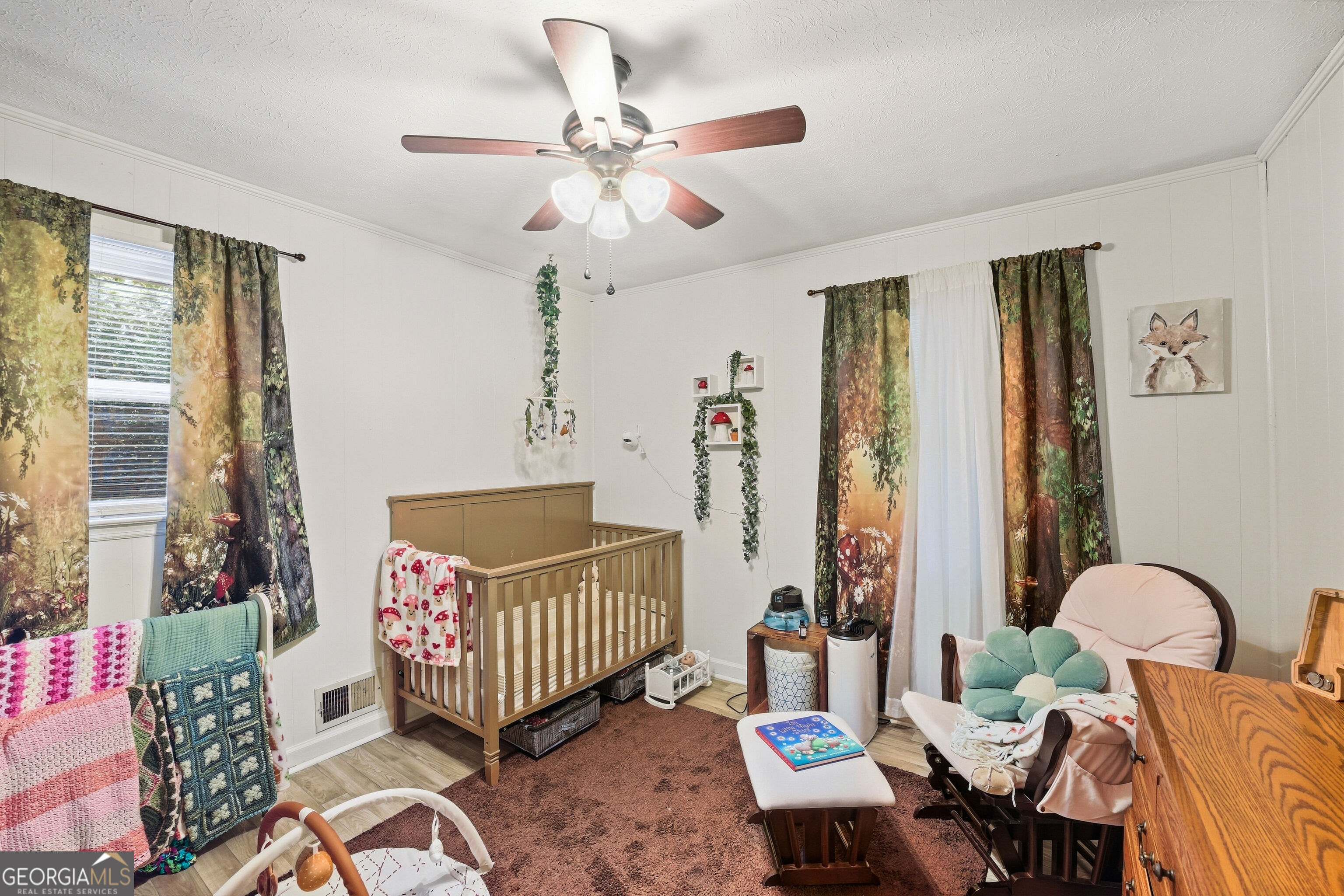 Furnished nursery with a wooden crib, woodland curtains, and a cushioned rocking chair.