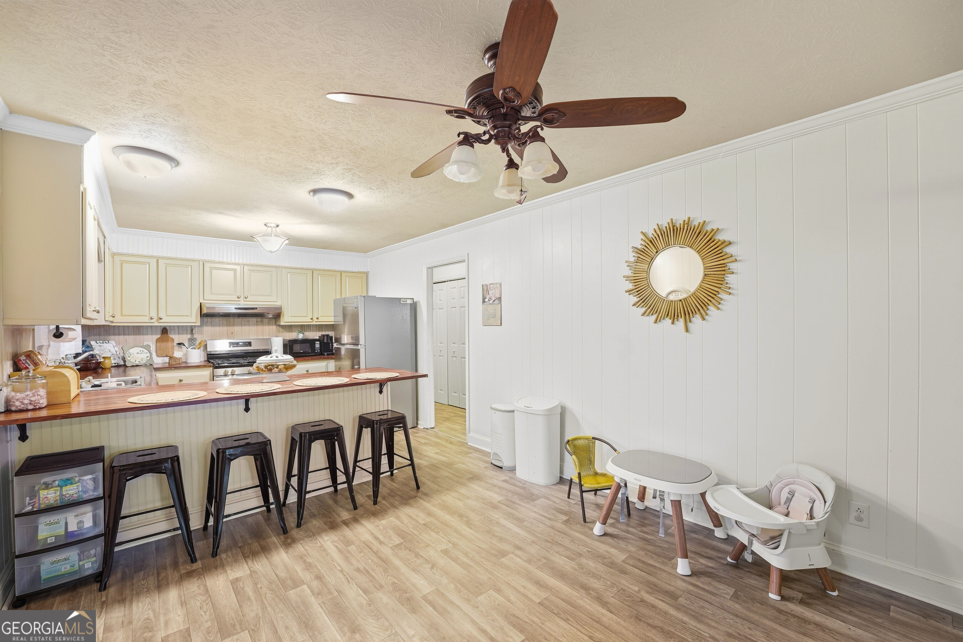 Kitchen with cream cabinets, a long breakfast bar and stools, and a small dining area with a high chair.