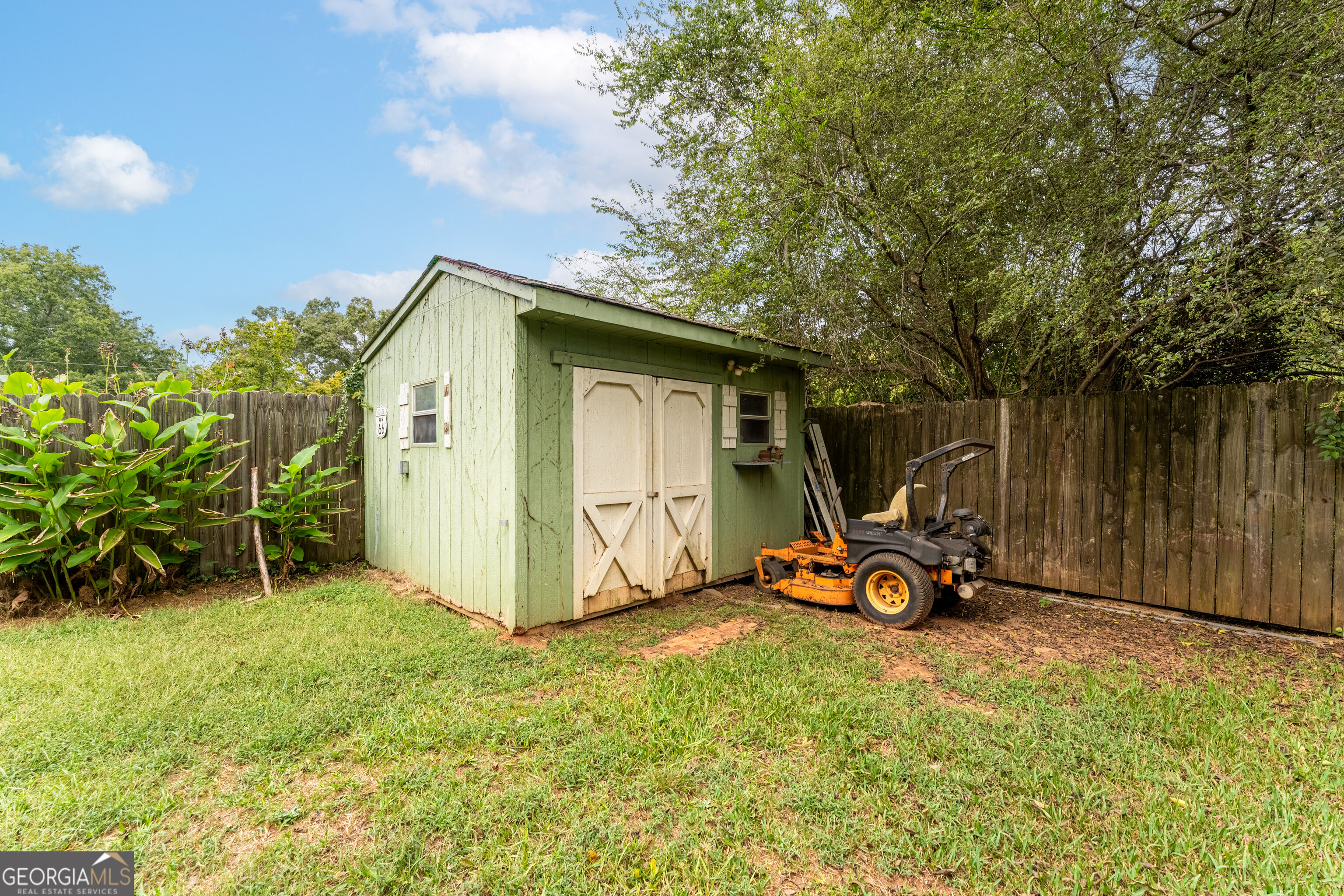 Pale green backyard shed with white double doors and a riding mower beside it.