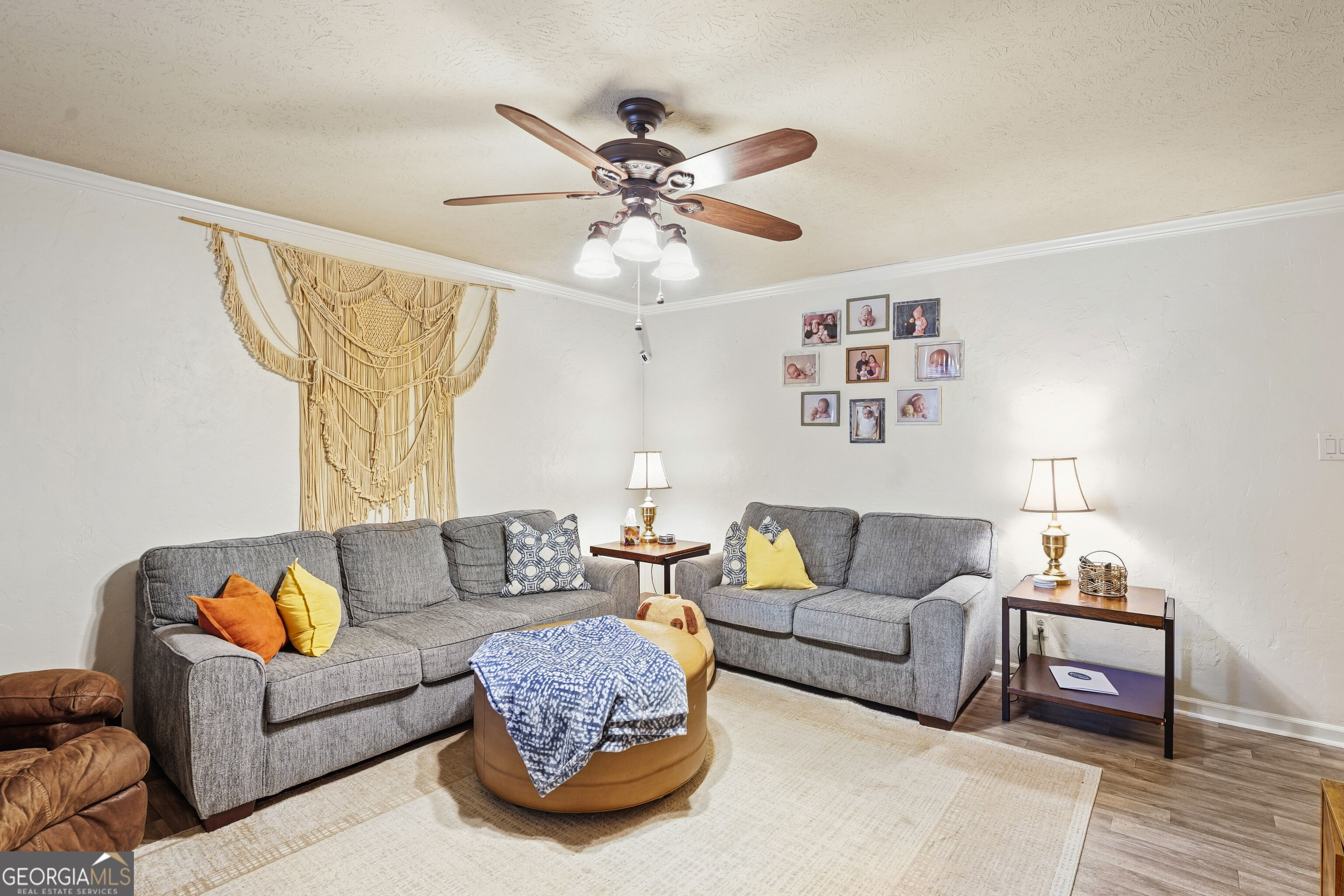 Living room with gray sofas, a blanket-covered ottoman, and a large macrame wall hanging.