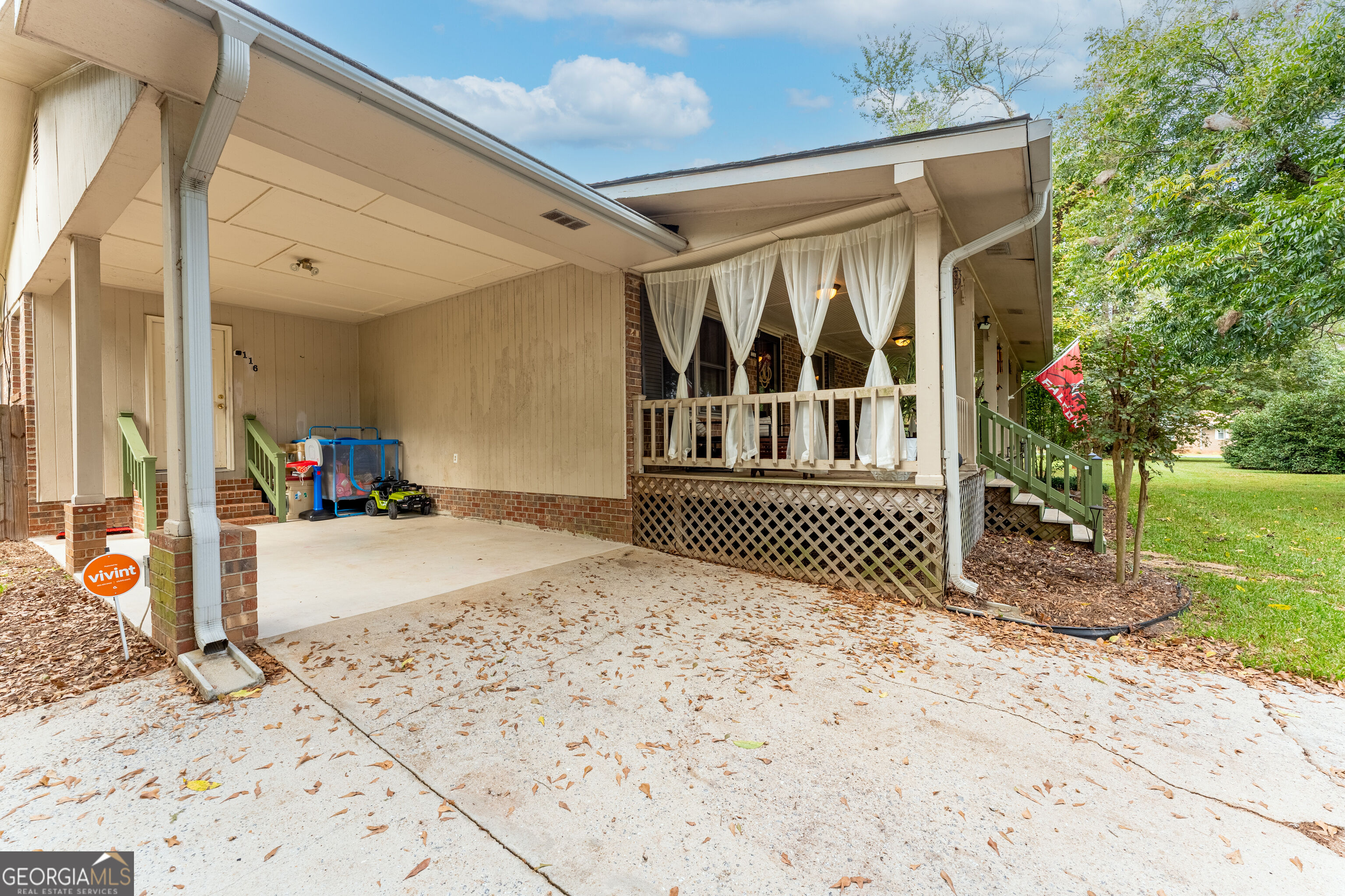 Covered porch with white curtains and green railings beside a broad concrete driveway.