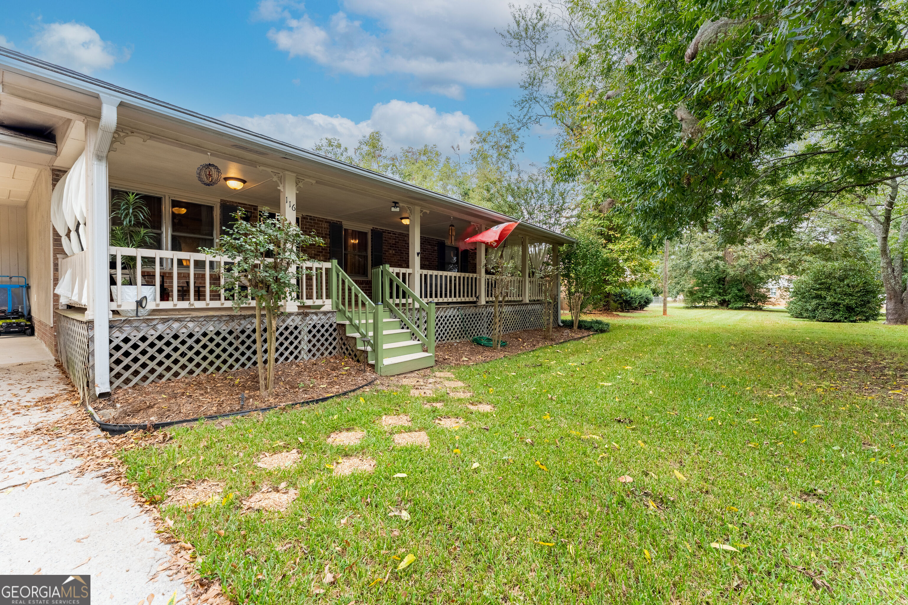 Brick home with a long covered porch, green steps, and a broad tree-lined lawn.