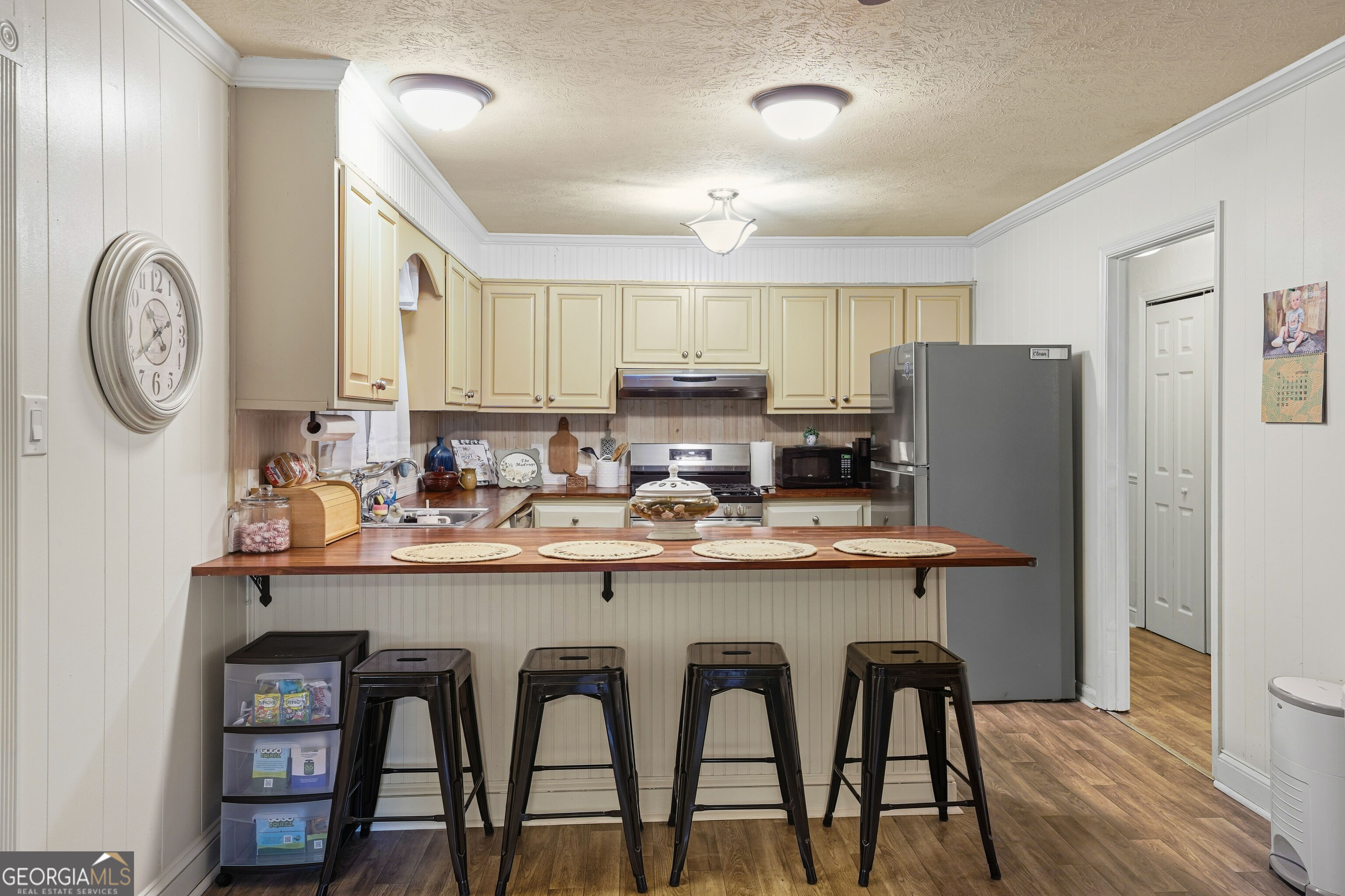 Kitchen with cream cabinets, stainless appliances, and a wood breakfast bar with four stools.