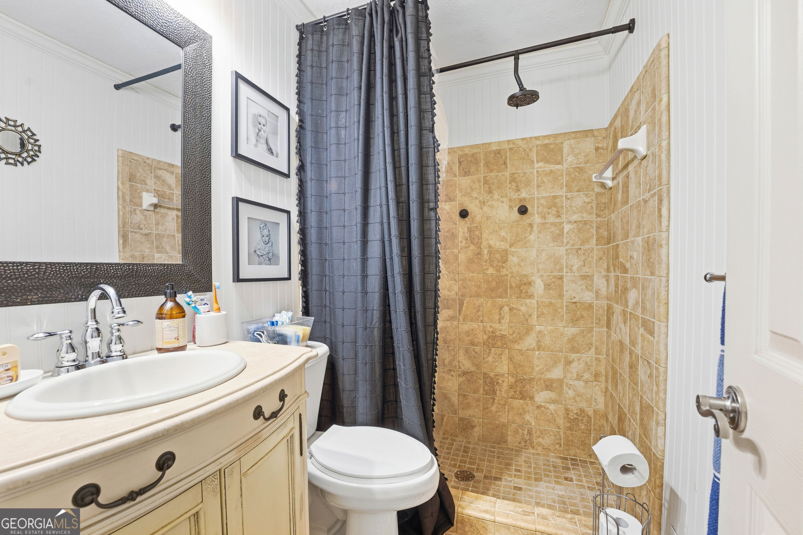 Bathroom with a tan tiled walk-in shower, dark curtain, cream vanity, and toilet.