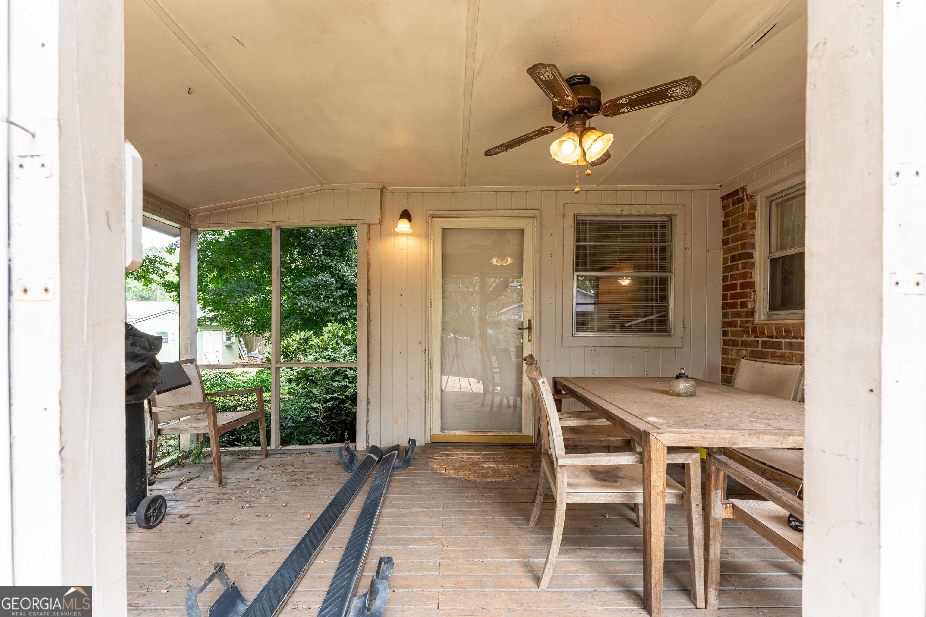 Screened porch with a wooden dining table, ceiling fan, and leafy views.