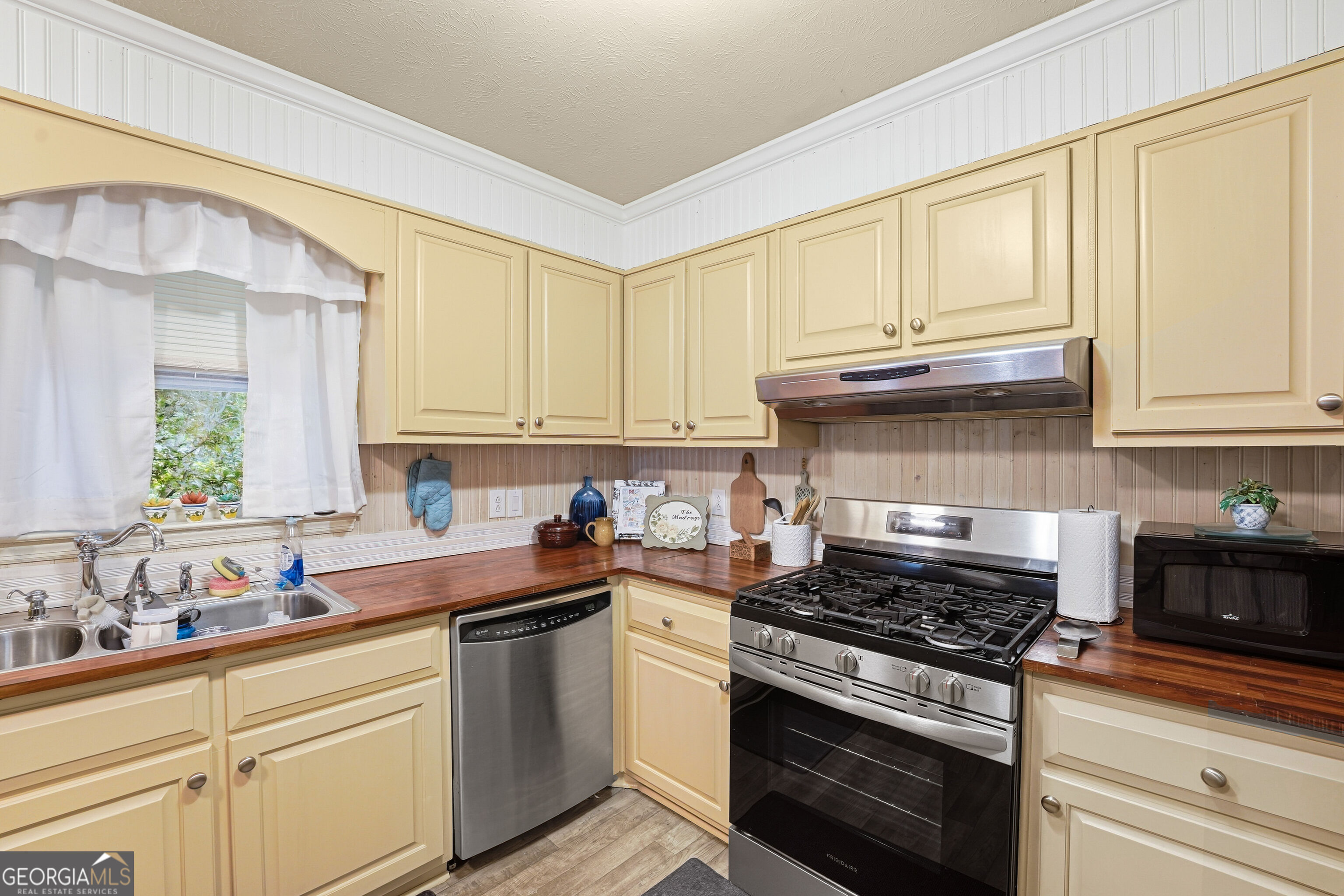 Kitchen with pale yellow cabinets, dark wood counters, and a stainless steel gas range.