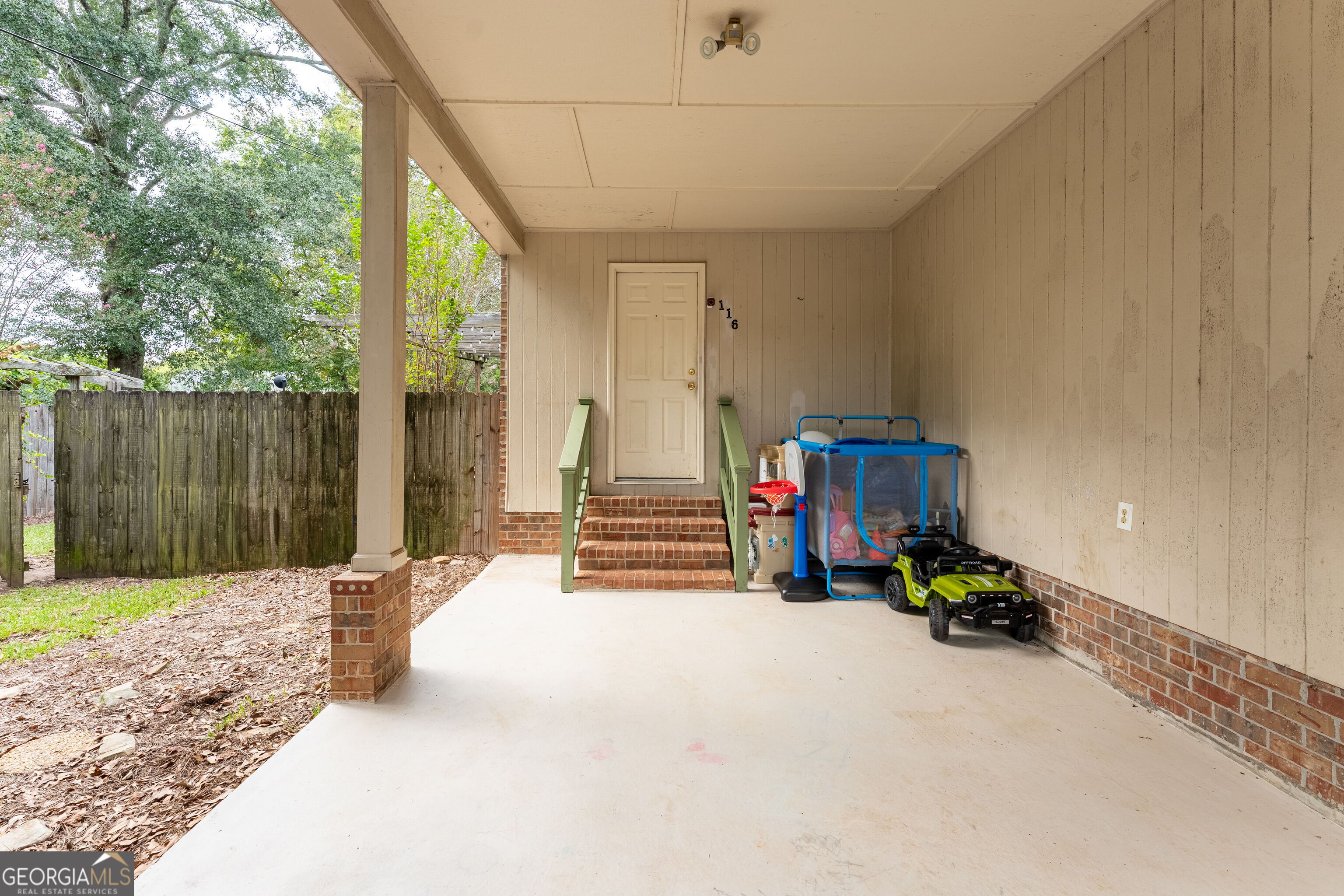 Covered porch with brick steps, green railings, a fenced yard, and children's play equipment.