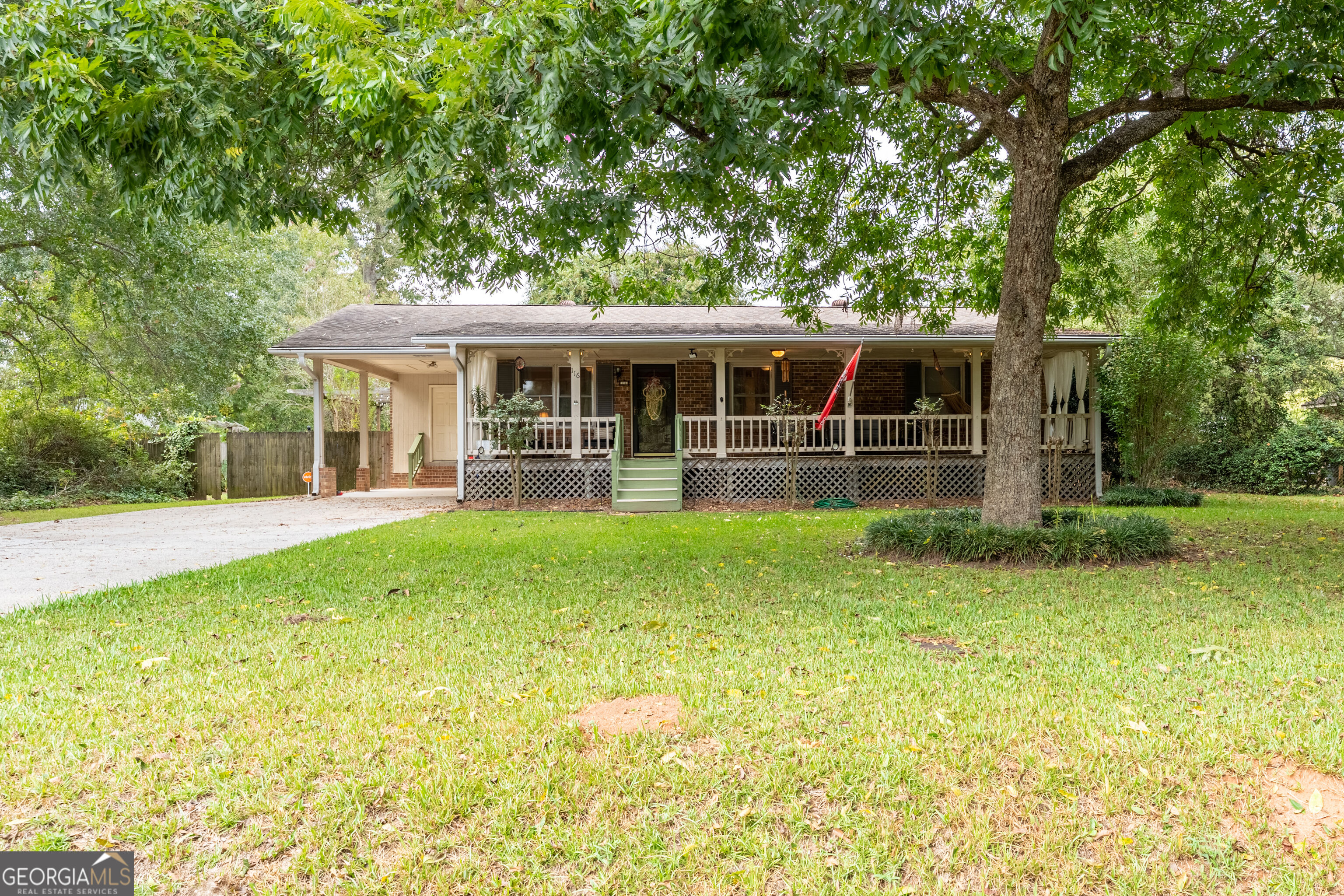 Single-story brick house with a wide covered porch beneath a large shade tree.