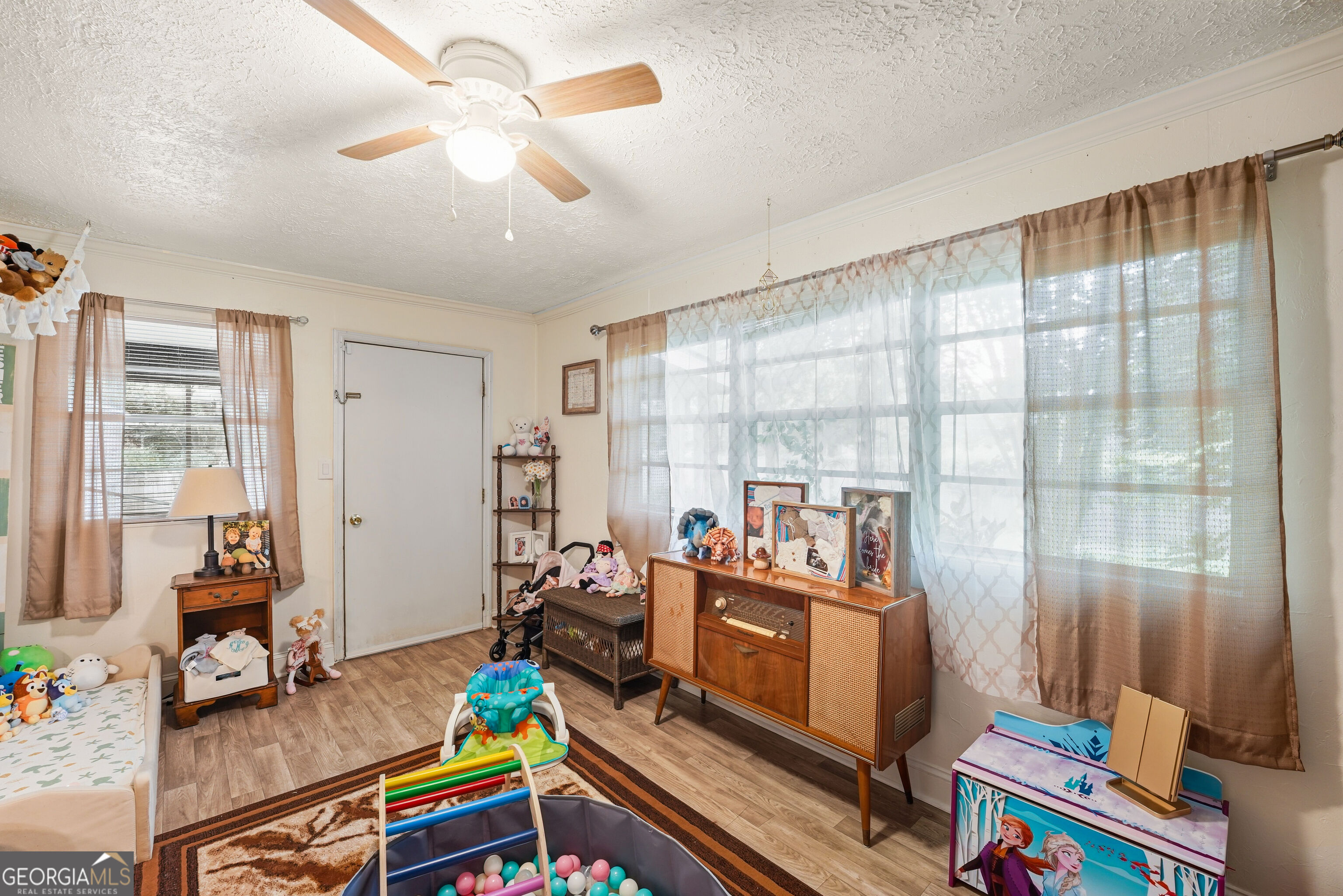 Child's bedroom with a large curtained window, toys, and a vintage wooden stereo cabinet.