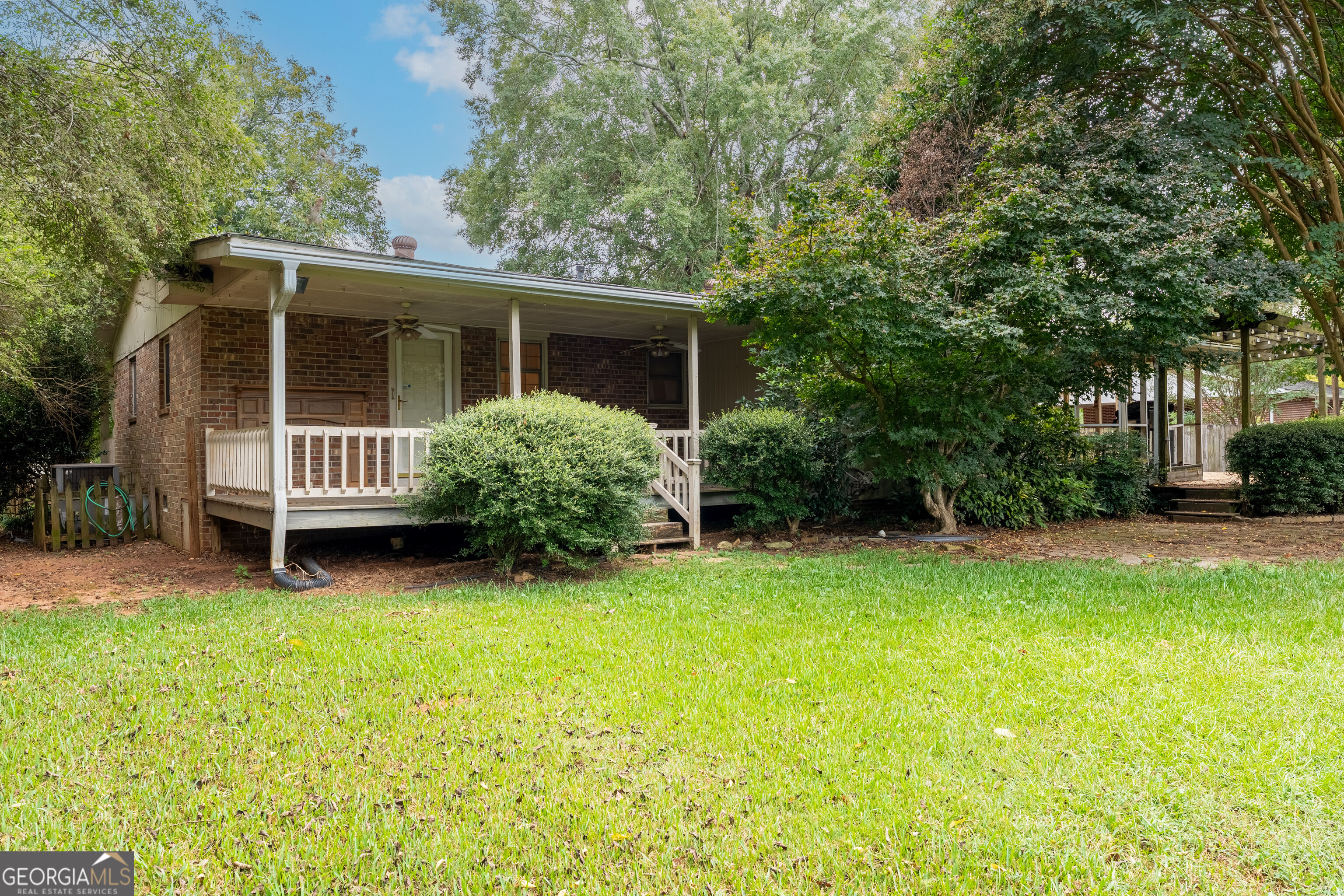 Brick home with a long covered porch, mature trees, and a broad green lawn.