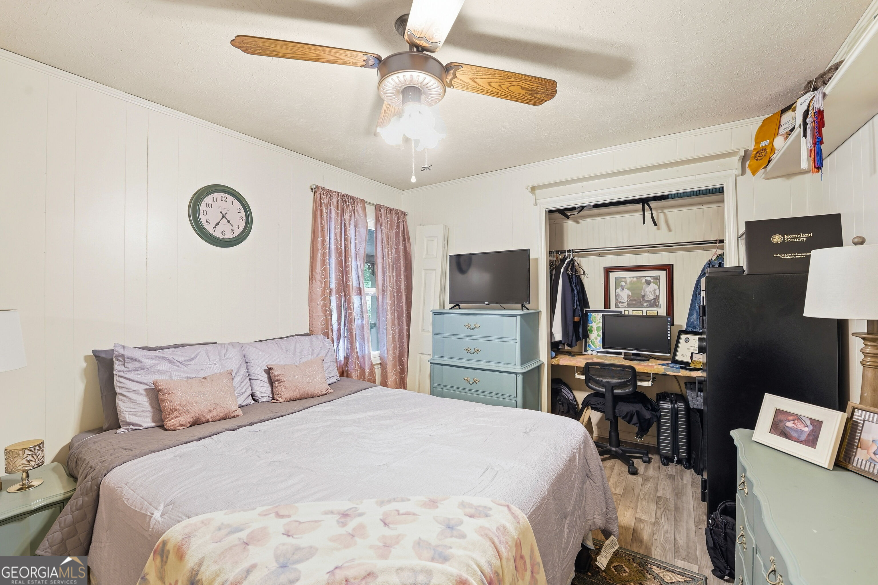 Furnished bedroom with a large bed, ceiling fan, and open closet with a computer workstation.