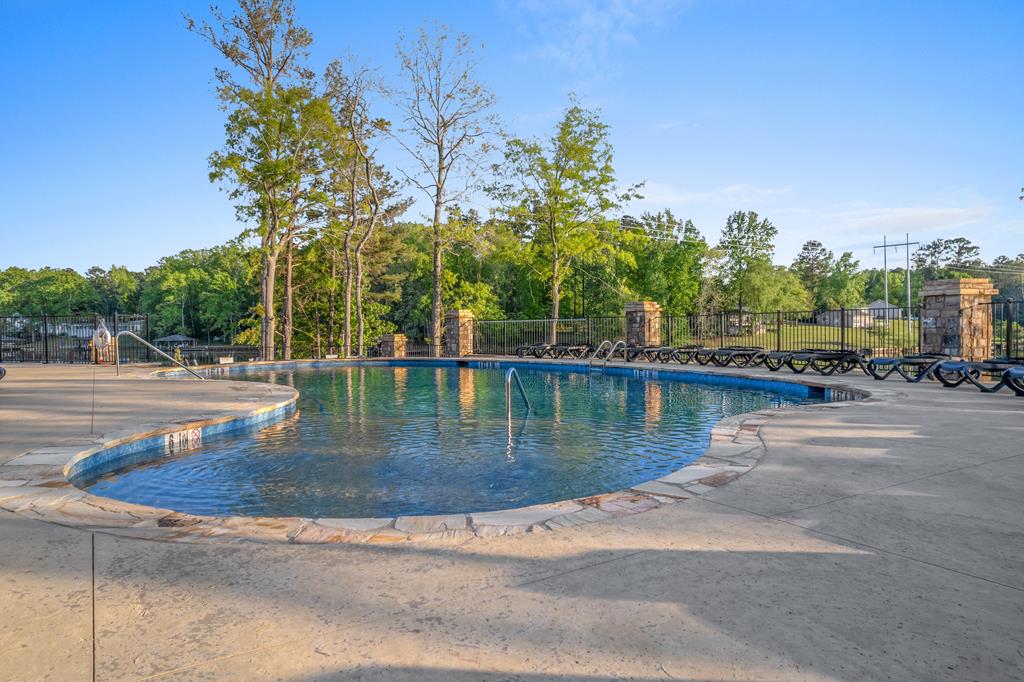Outdoor pool with a curved edge, lounge chairs, and trees behind a metal fence.
