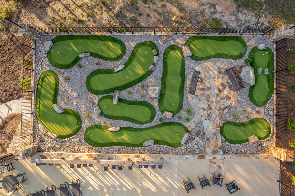 Aerial view of a miniature golf course with winding greens, stone paths, and a patio.