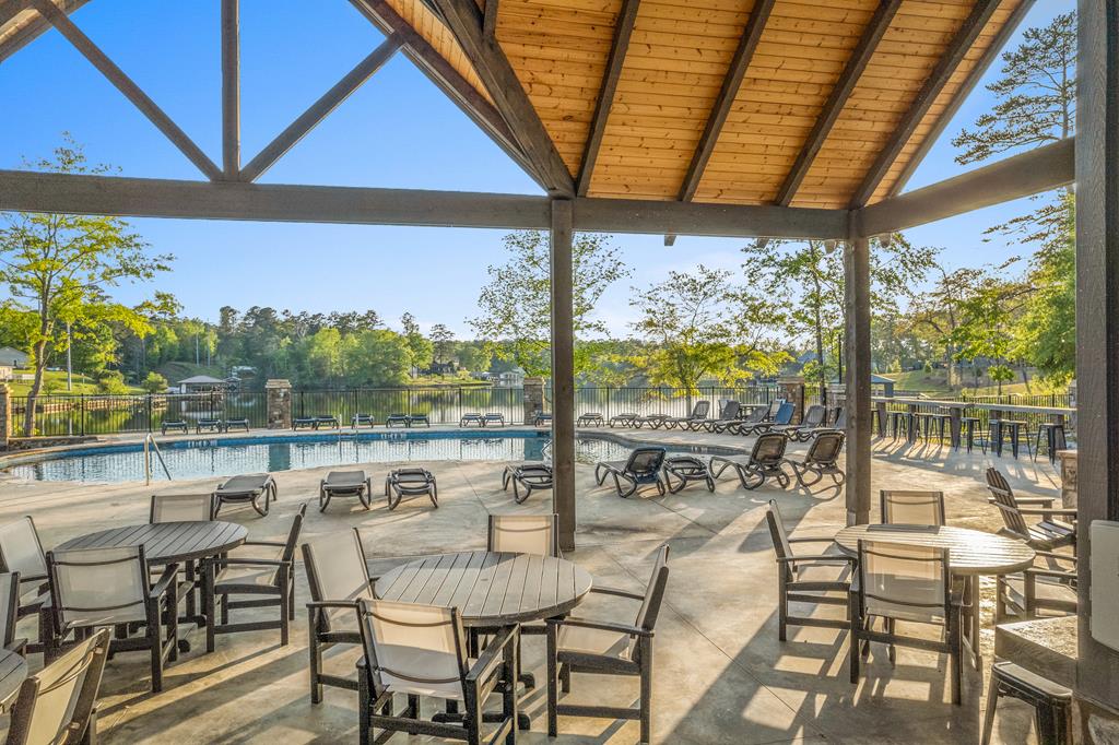Covered poolside pavilion with tables and chairs overlooking a pool and lake.