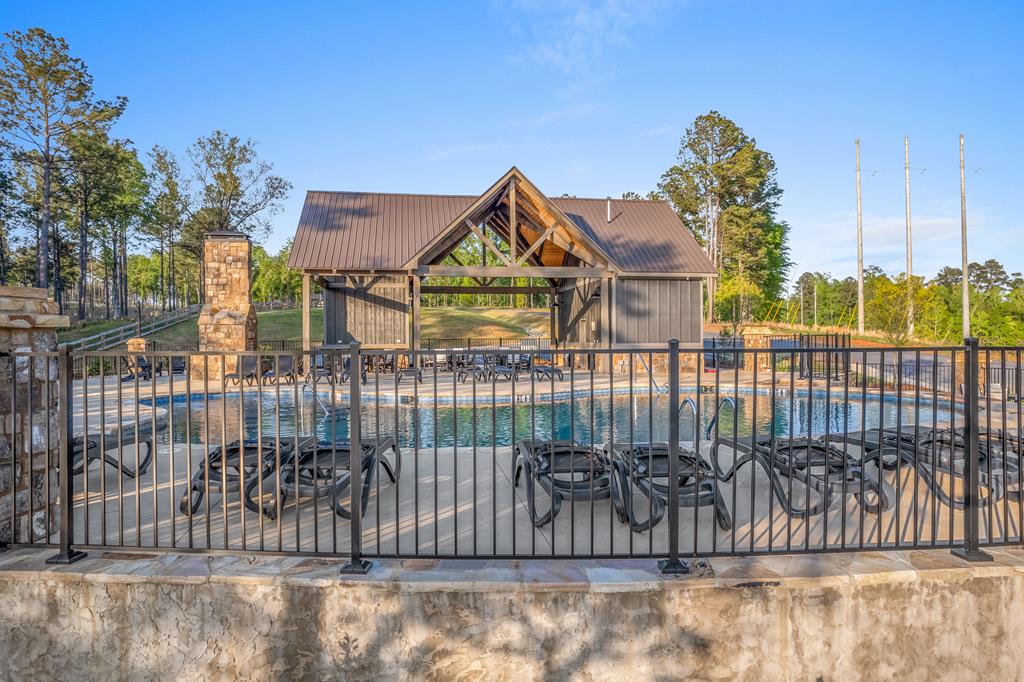Outdoor pool with lounge chairs and a timber pavilion behind a black metal fence.
