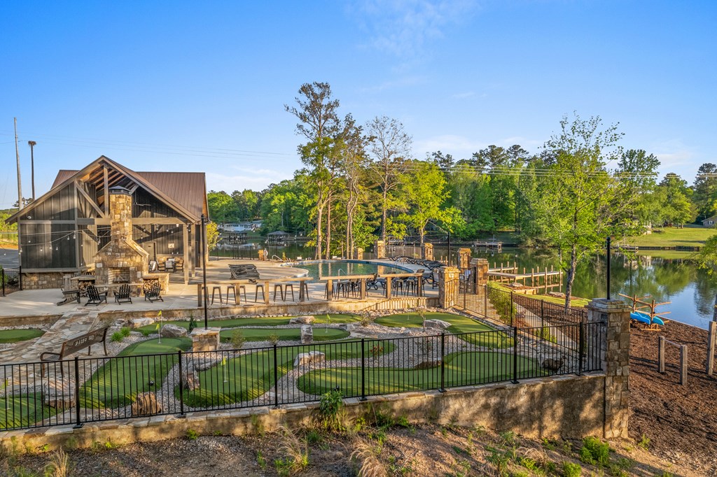 Lakeside clubhouse and outdoor pool with patio seating and a landscaped putting green.