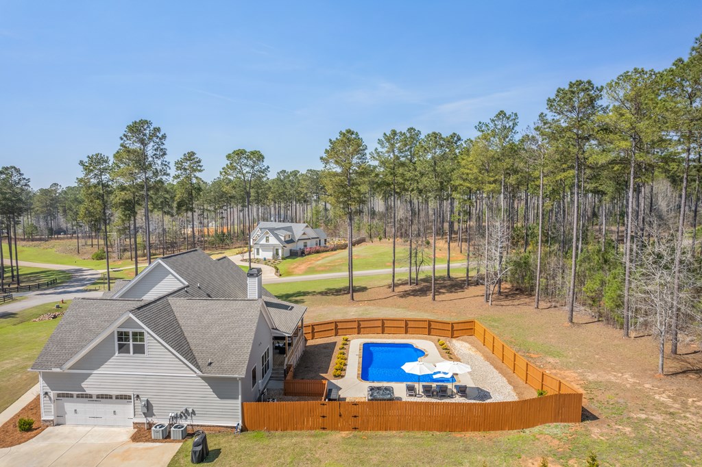 Aerial view of gray home with fenced swimming pool and wooded surroundings.
