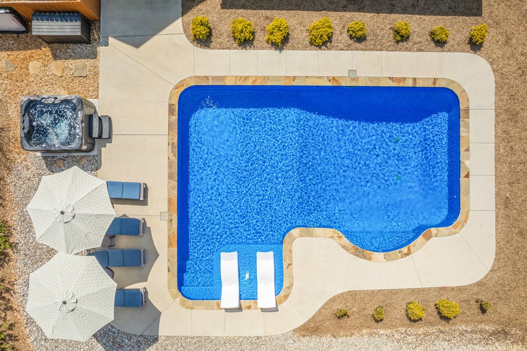 Swimming pool with two in-pool loungers, a surrounding stone deck, and a nearby hot tub.