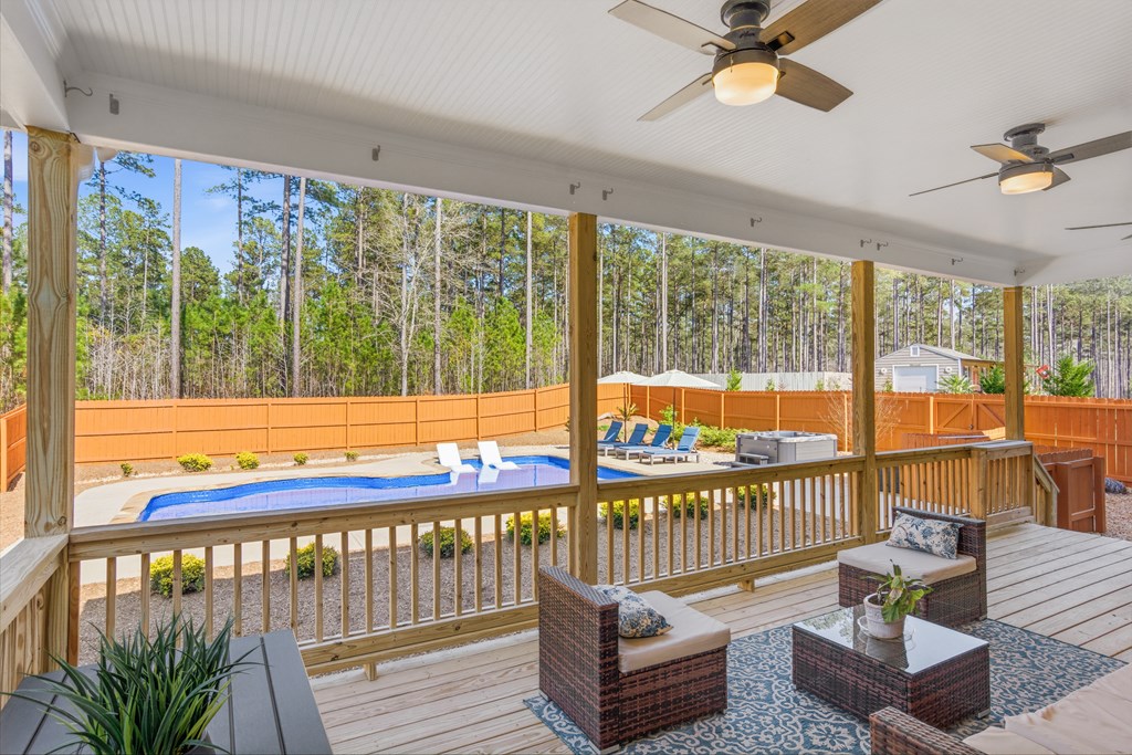 Covered wooden deck with wicker seating overlooks a backyard pool and wooded surroundings.