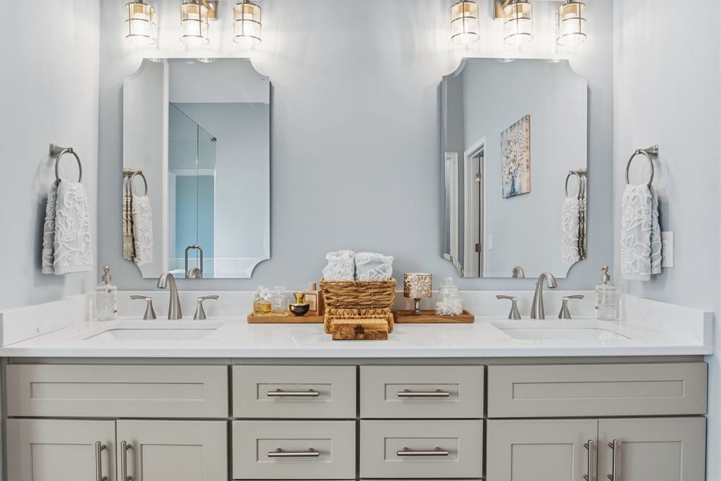 Bathroom double vanity with two framed mirrors, light gray cabinetry, and neatly arranged towels.