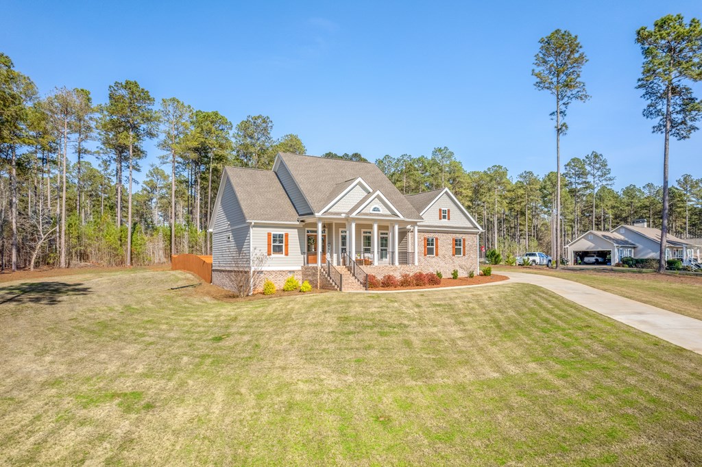 Single-story home with a covered porch and brick accents, surrounded by lawn and pine trees.