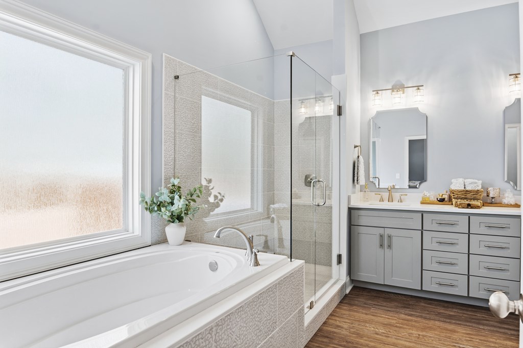 Bathroom with a soaking tub, glass shower, gray double vanity, and large window.